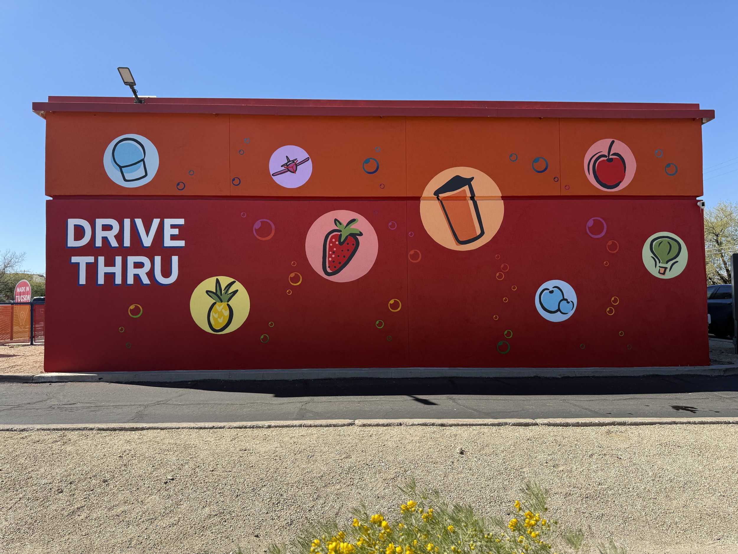 Bright red wall with colorful icons of fruits, drinks, and food, and the words 'DRIVE THRU' in large white and blue letters.