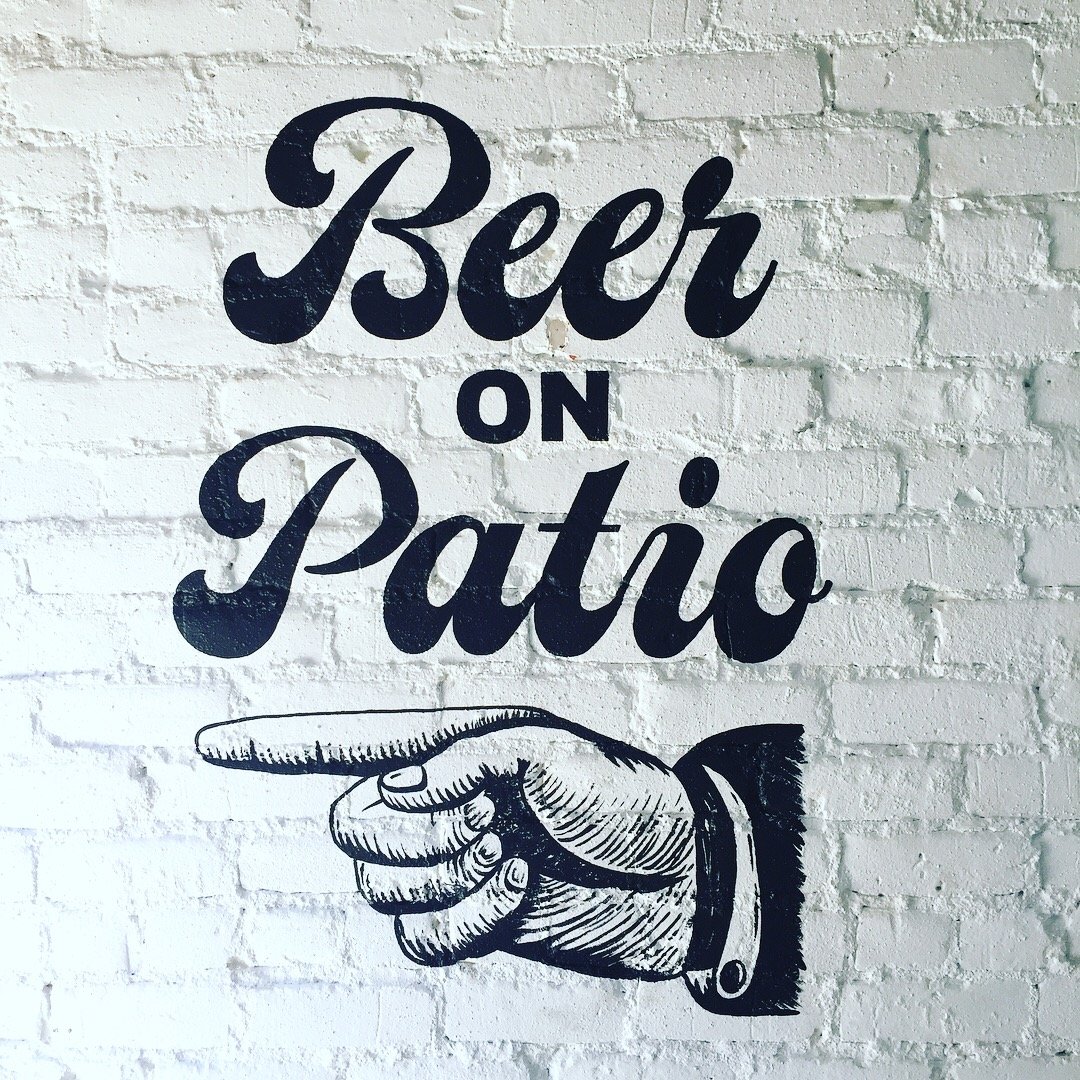 Wall art with the phrase 'Beer on Patio' in bold, cursive font and an illustration of a pointing hand in black and white.
