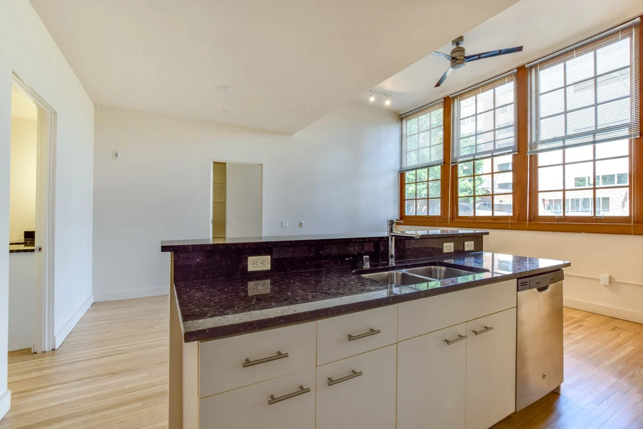 Kitchen with a dark granite countertop island, white cabinetry, large windows with blinds, a ceiling fan, and light wood flooring.