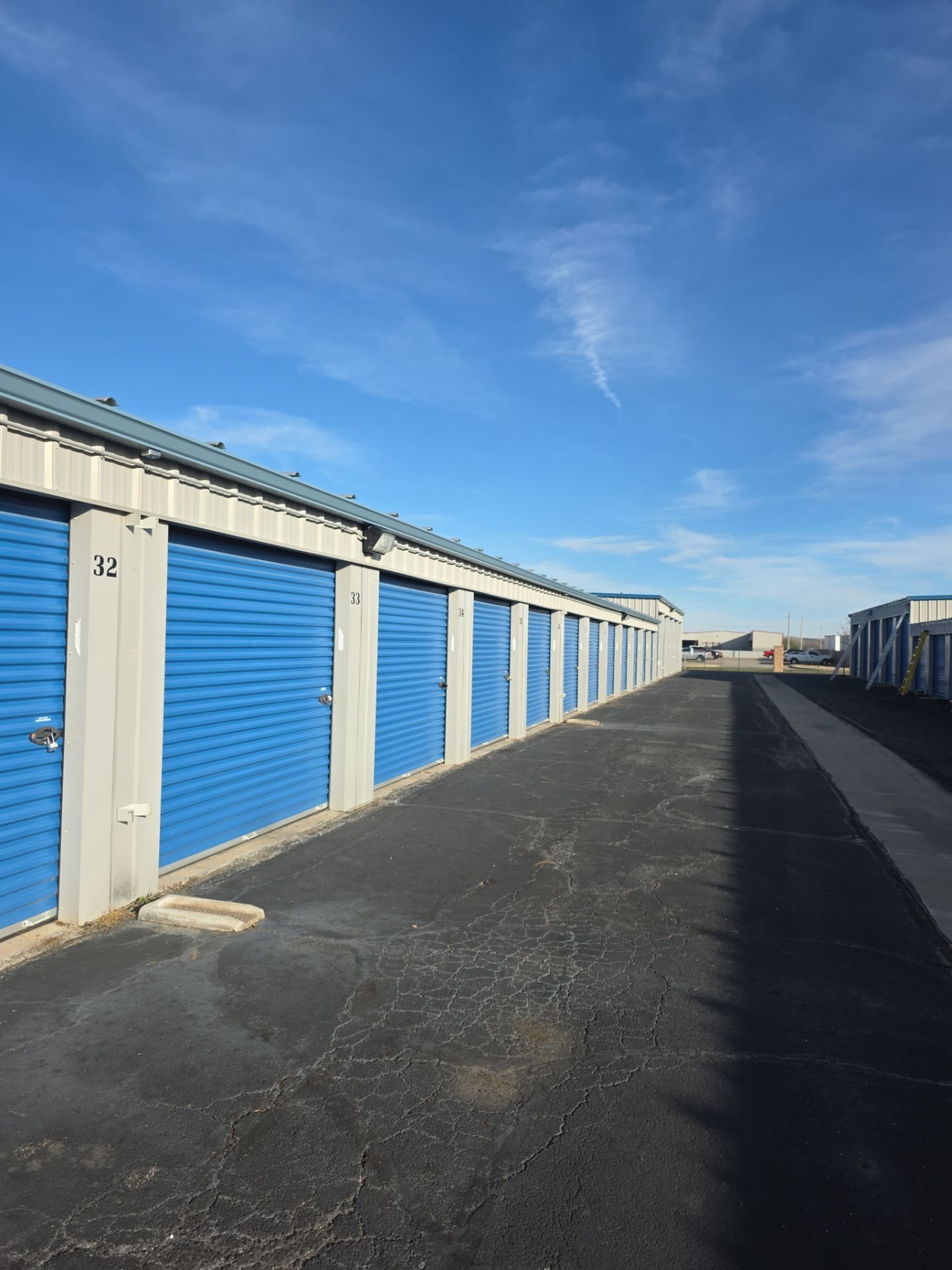 Row of storage units with blue doors, numbered 32 to 34, in an outdoor storage facility under a partly cloudy sky.
