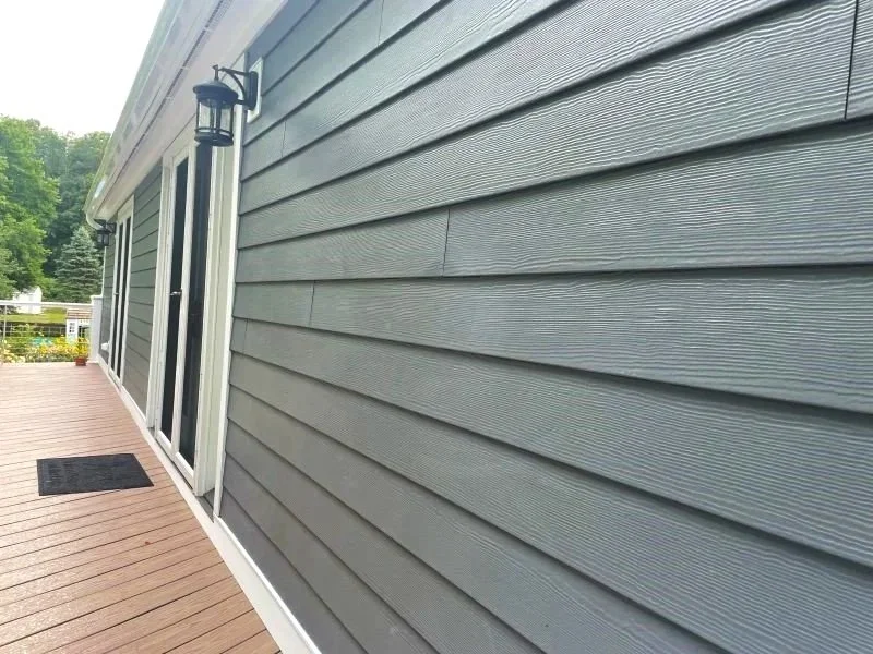 Exterior view of a house with horizontal gray vinyl siding, a sliding glass door, two black outdoor wall lanterns, and a wooden deck with a black doormat.