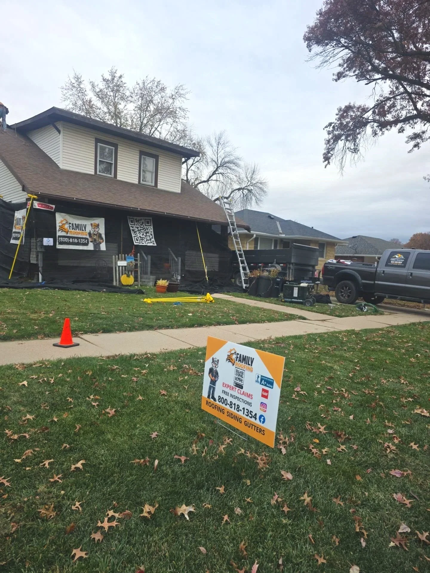 Residential street with house undergoing roofing work, ladder leaning against the house, and a sign in front advertising roofing services, including free inspections, with contact information.