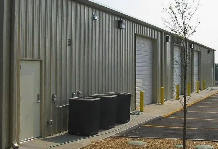 Exterior view of a metal warehouse with three roll-up doors, a small side door, and parking spaces in front.
