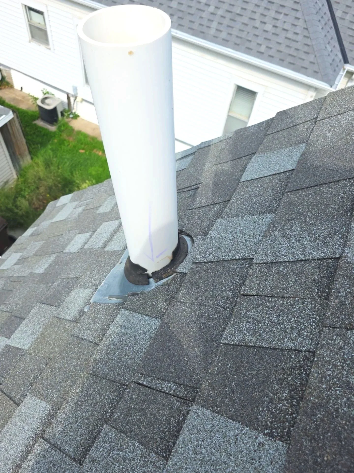 A close-up of a roof vent pipe protruding from asphalt shingle roofing, with a white pipe and metal flashing installed around it.