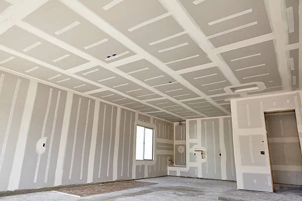 Interior of a room under construction with drywall installed, visible joints, a window, and a doorway.