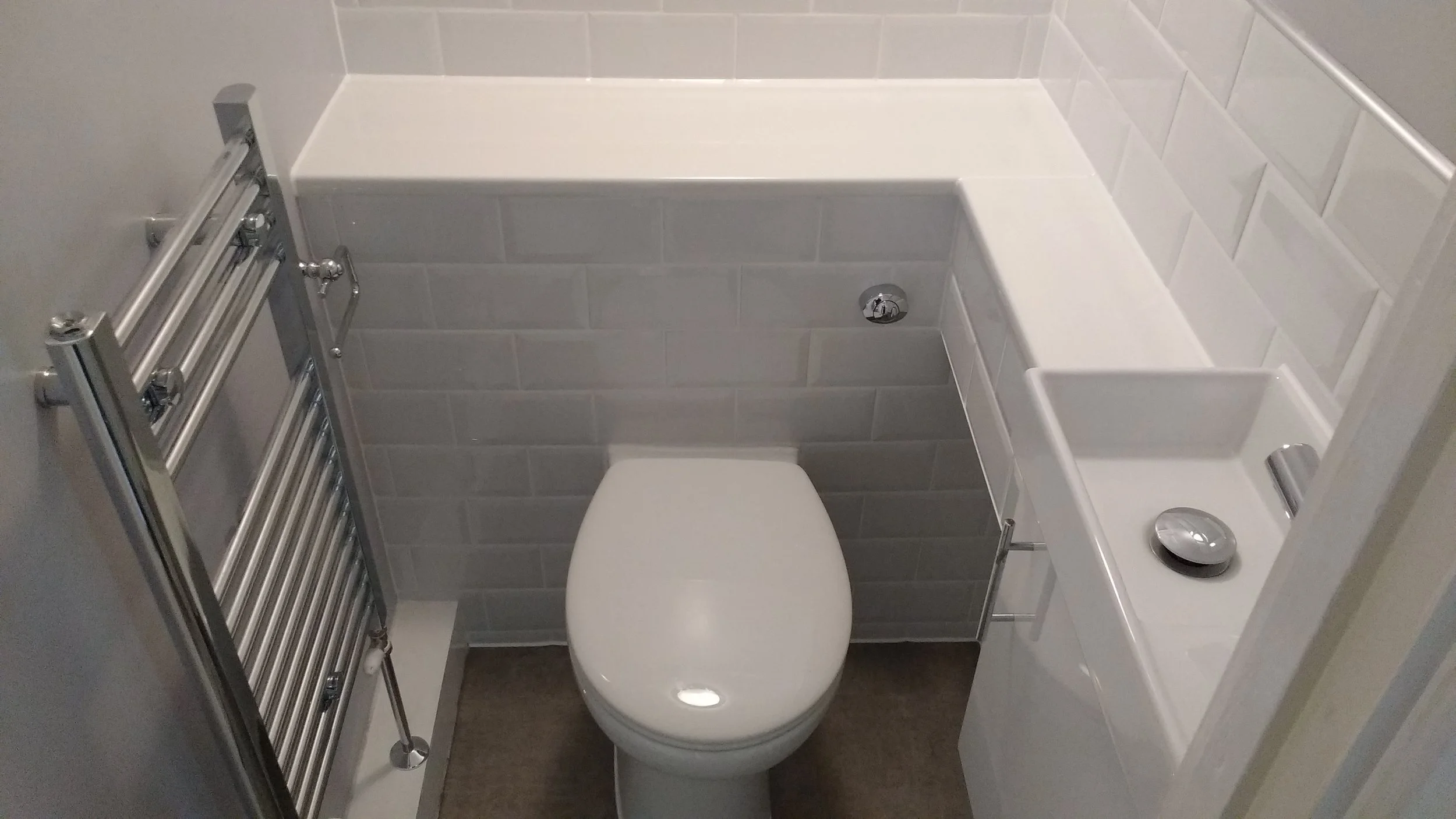 Small bathroom with toilet, white sink, gray tiled walls, and chrome towel radiator.