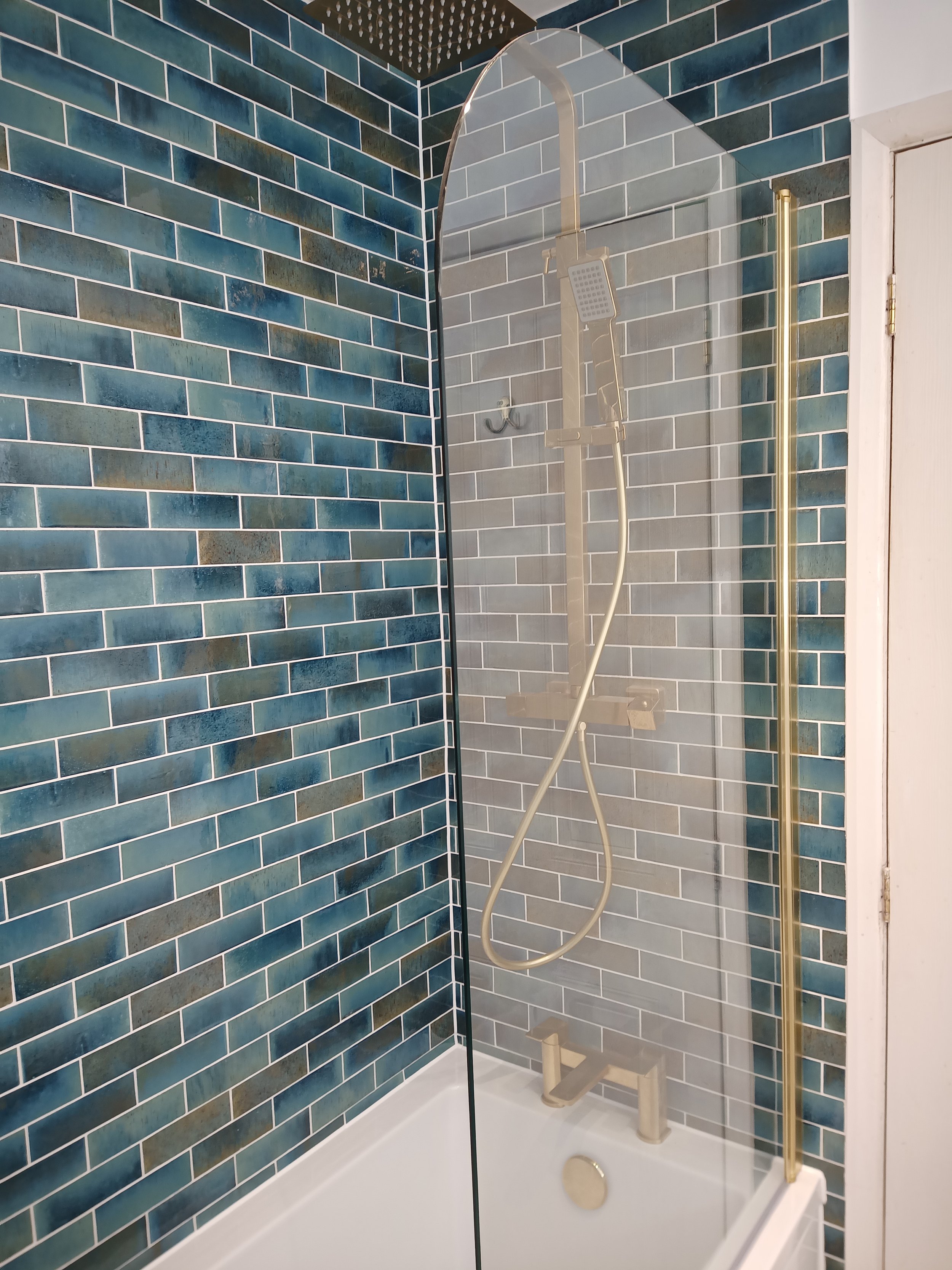 Bathroom shower with blue tile walls, a glass partition, and a brass showerhead with handheld attachment.