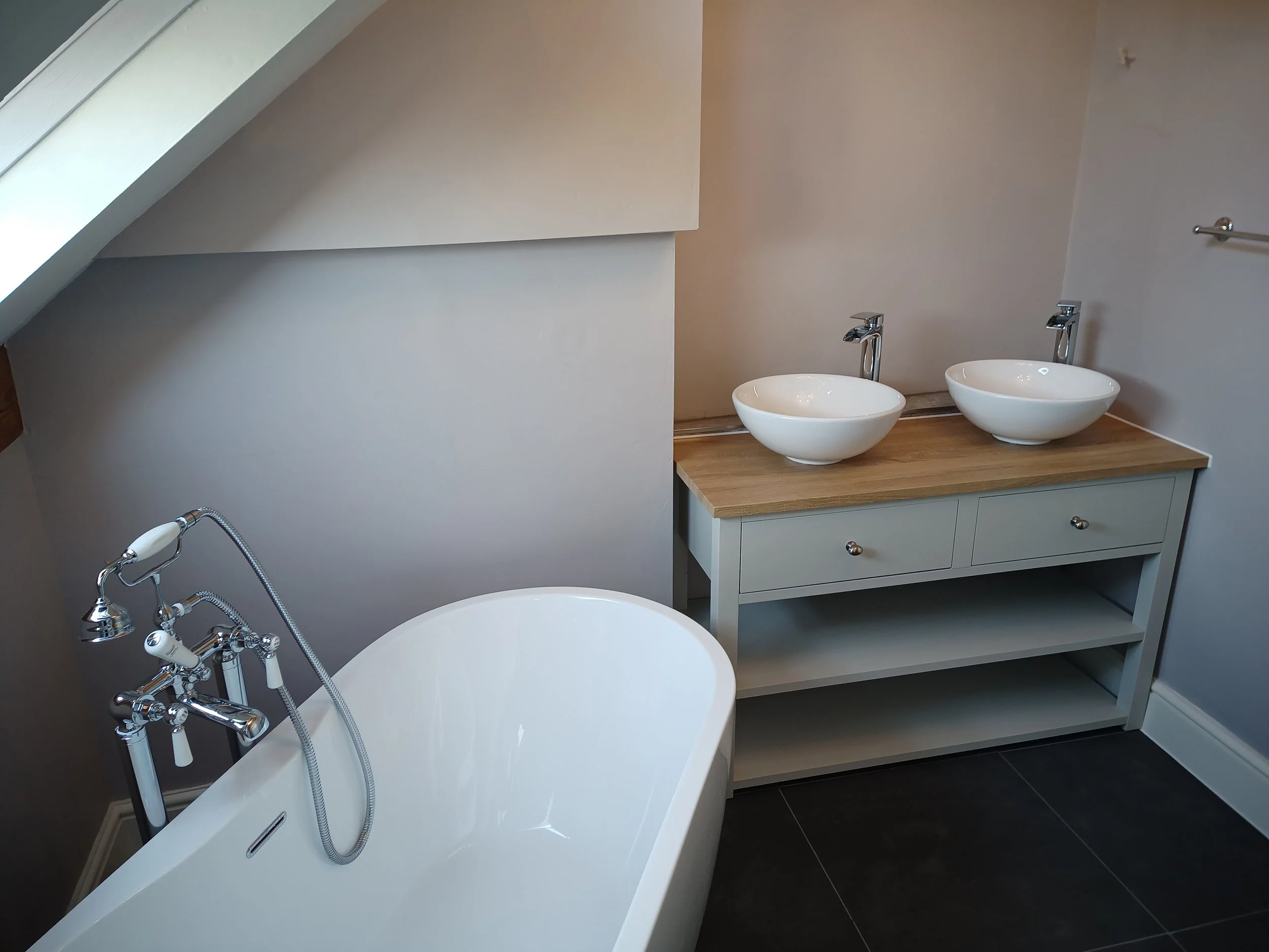 Bathroom with a white bathtub, a vanity with two vessel sinks, and a skylight window.