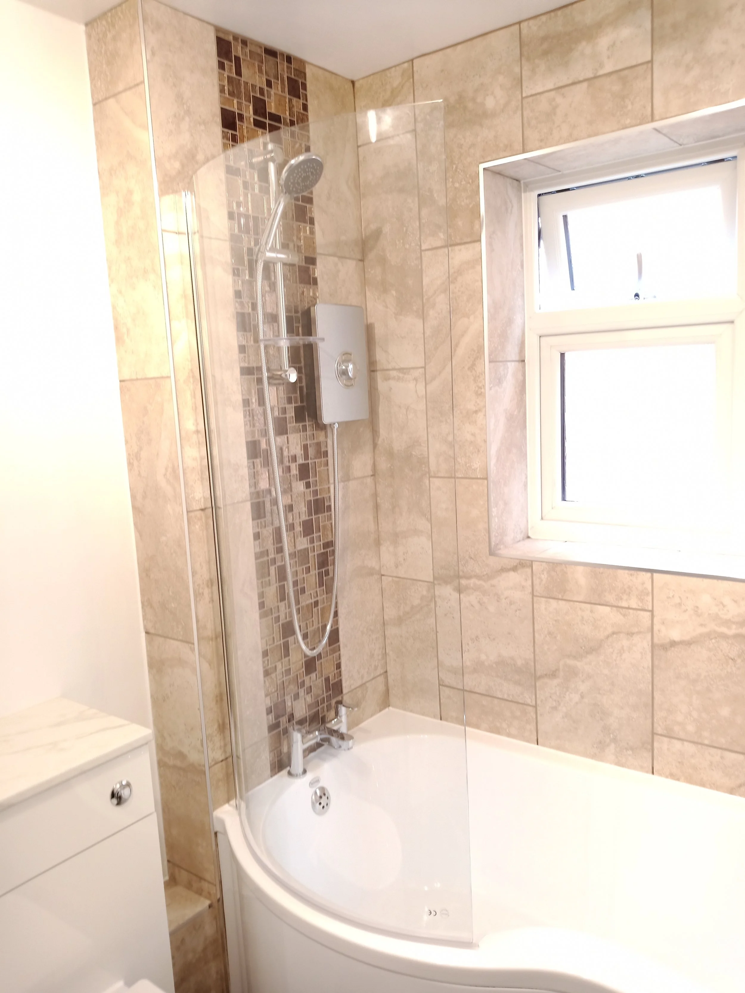 Bathroom with tiled walls and a corner bathtub with a glass shower screen and a window.