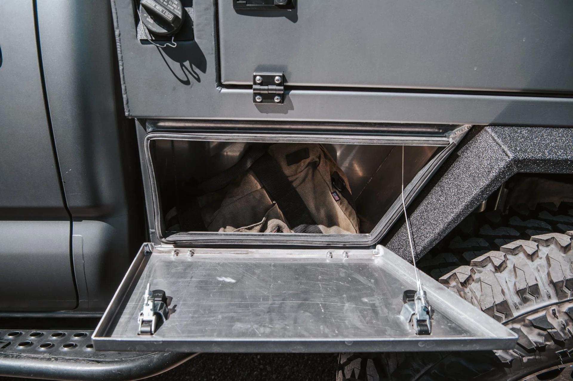 Open metal compartment on a vehicle with a tan bag inside.