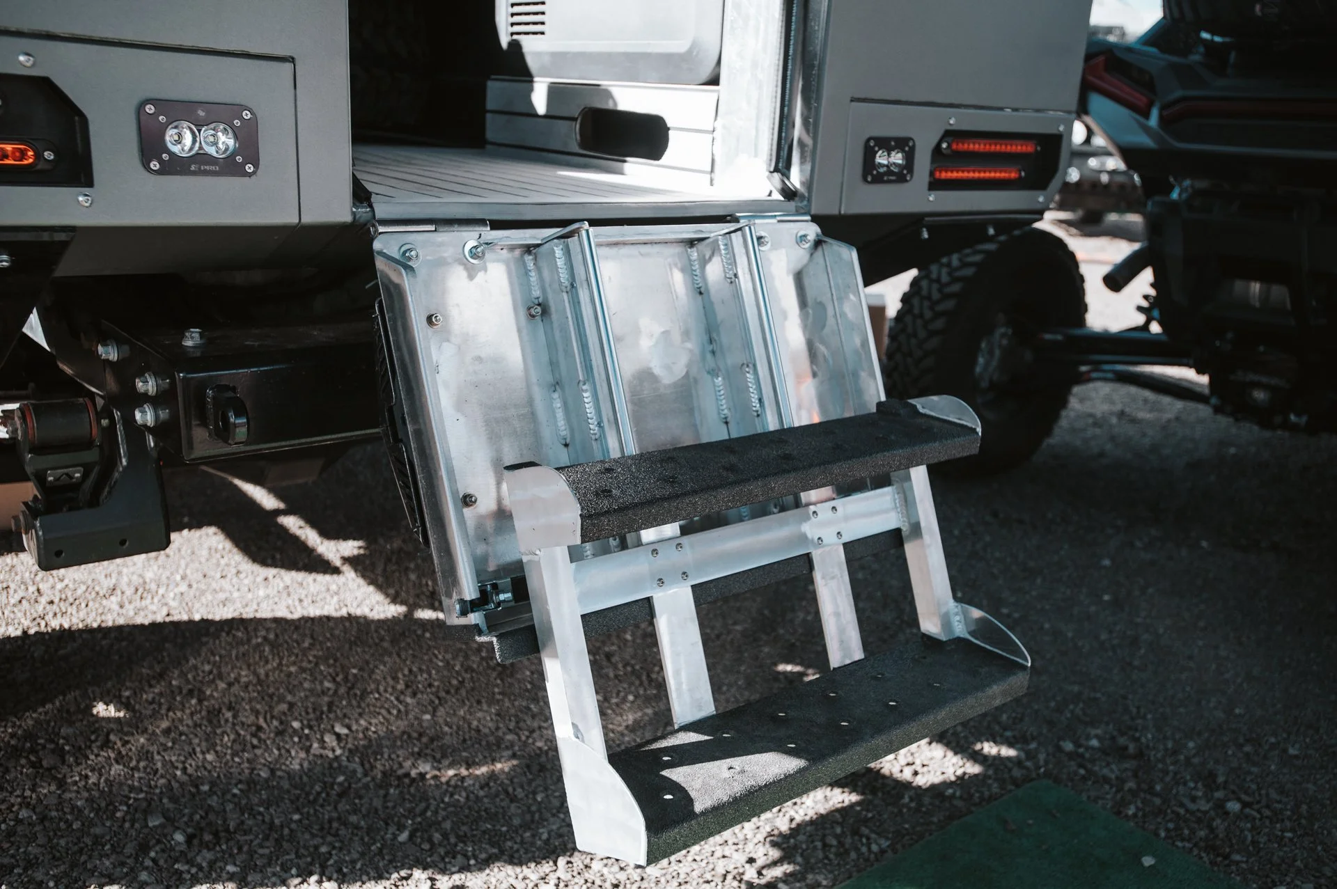 Close-up of a mechanical wheelchair lift attached to an off-road vehicle with large tires, showing steps and metal components.