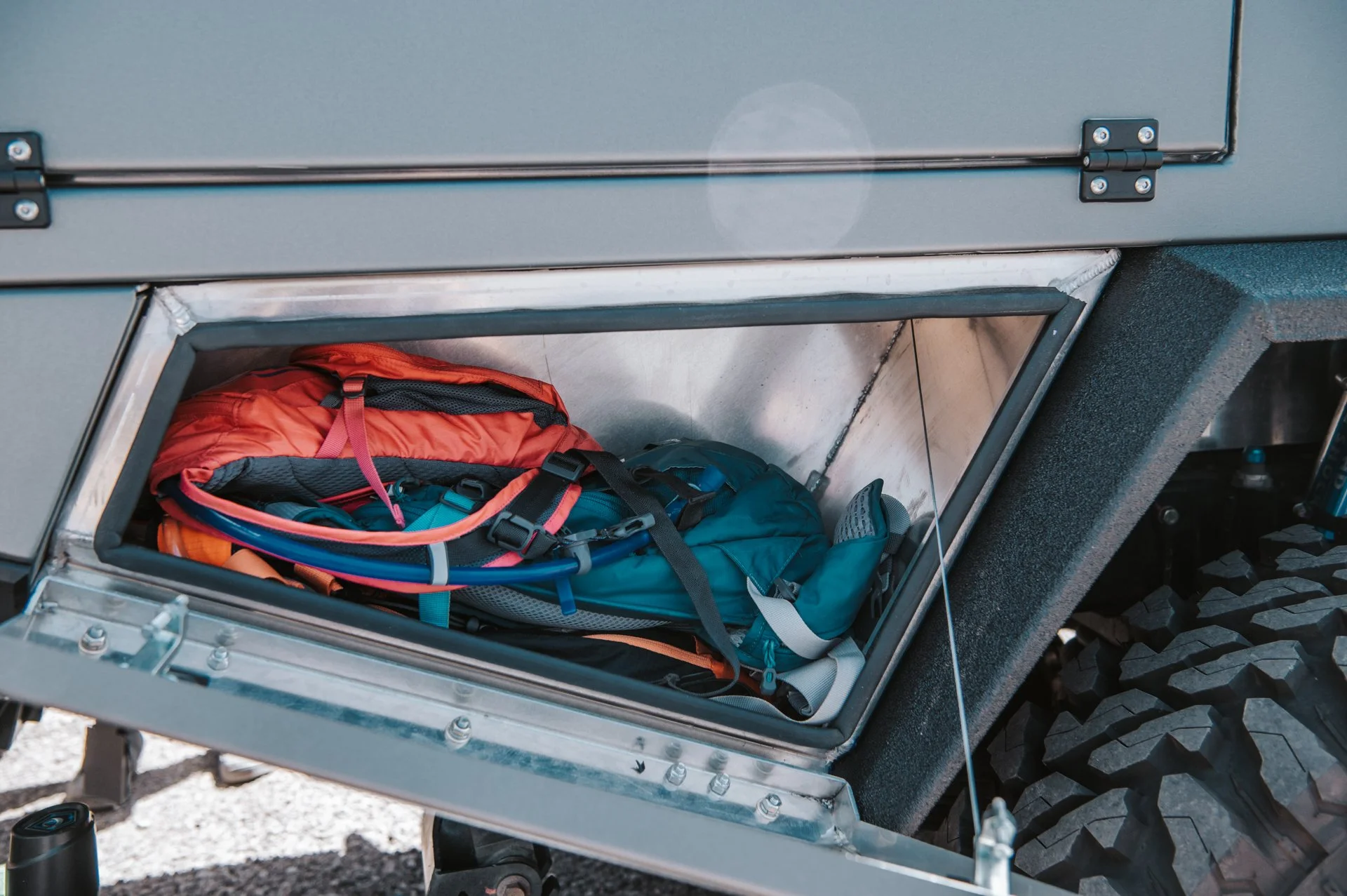 Open storage compartment on a rugged off-road vehicle containing a red backpack, a blue backpack, and some hoses or tubes.