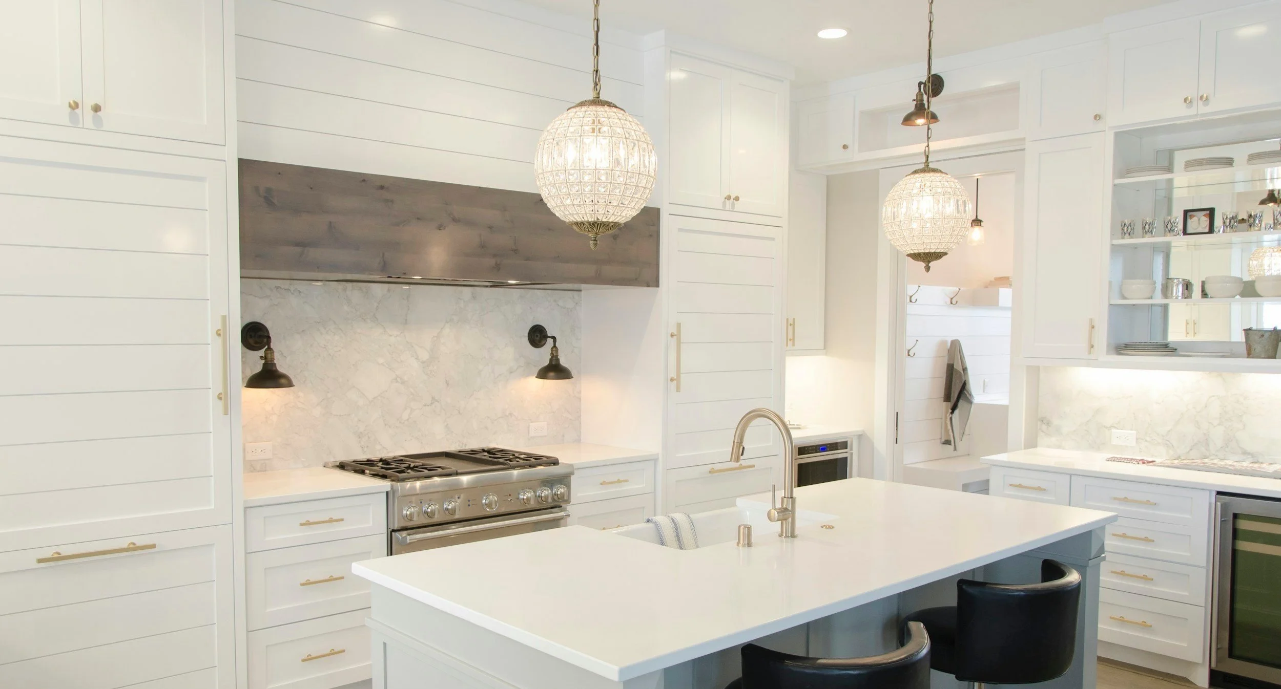 Modern white kitchen with marble backsplash and island, pendant lighting, built-in appliances, and open shelving.