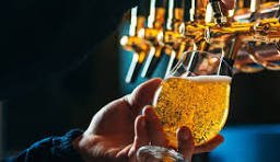 A hand holding a glass of beer under beer taps in a bar or brewery.