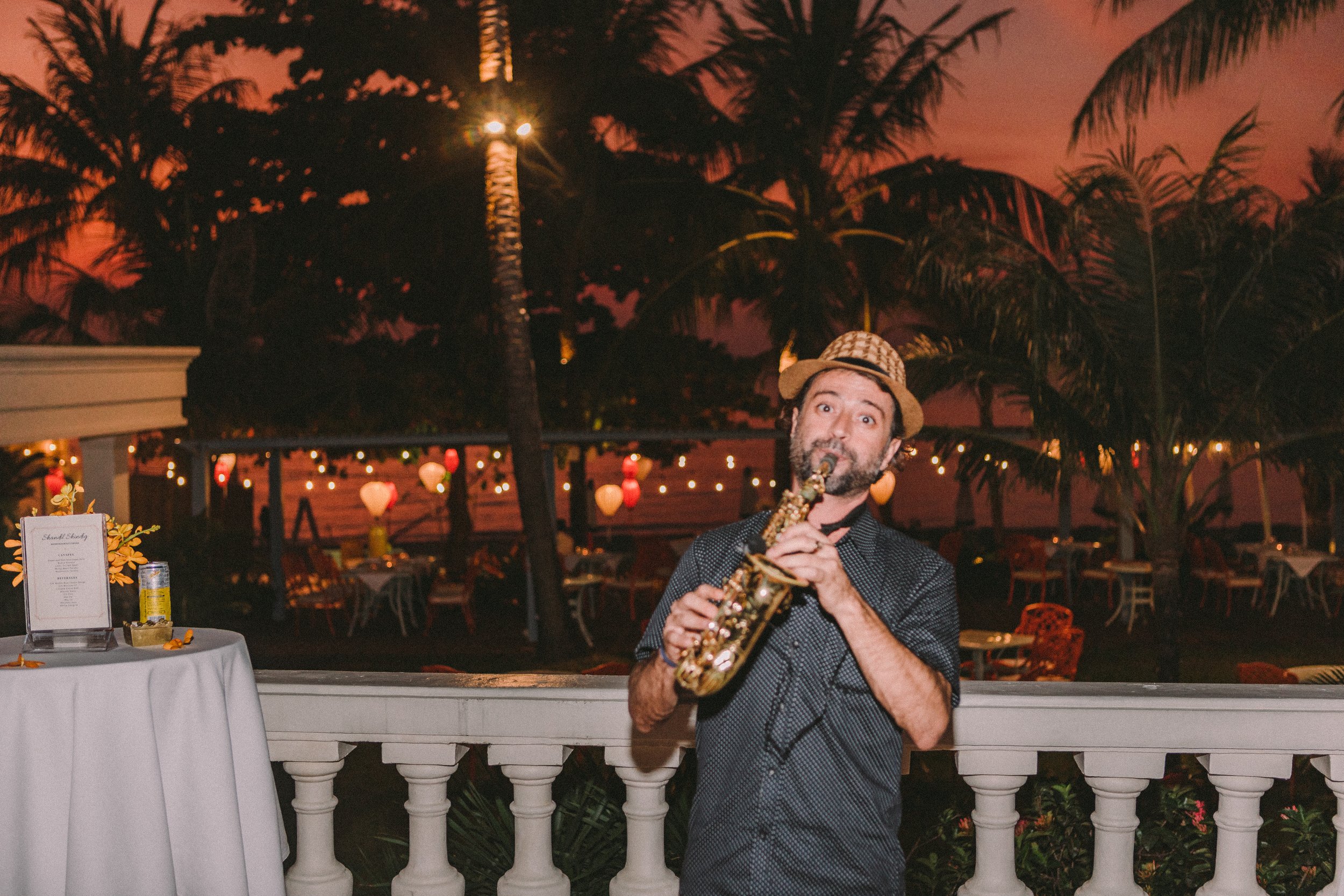Musician playing saxophone at a sunset event, framed by palm trees and ambient string lights. Captured by Maksym Brukhno for lifestyle and hospitality event coverage.
