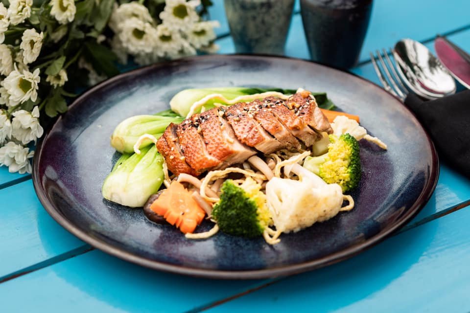 Gourmet salmon plate with steamed broccoli, cauliflower, carrots, and bok choy on a modern blue table. Styled and photographed by Maksym Brukhno for restaurant campaigns.