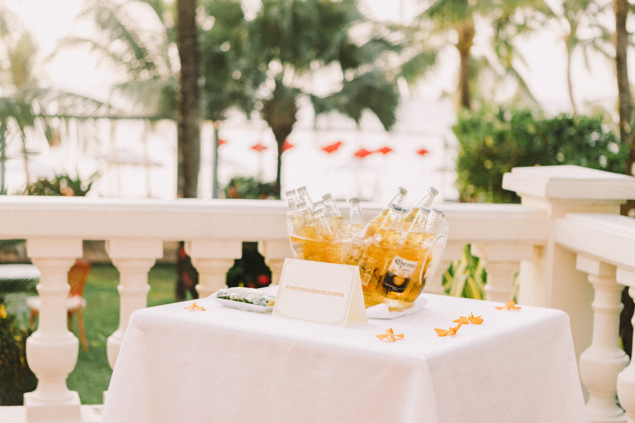 Outdoor horeca branding shot — buckets of Corona beer on a styled event table with branded signage and a leafy green backdrop. Captured by Maksym Brukhno for hospitality and event marketing.