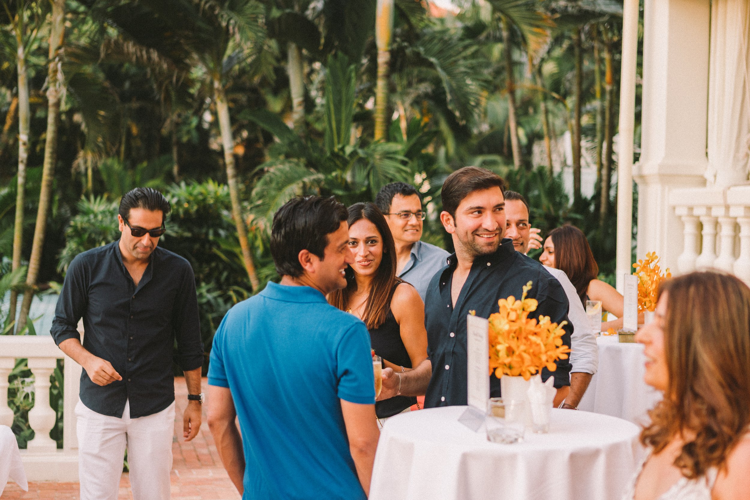 Lively outdoor gathering photo by Maksym Brukhno — people mingling near a tropical courtyard with white walls and lush greenery. Hospitality lifestyle and event photography.