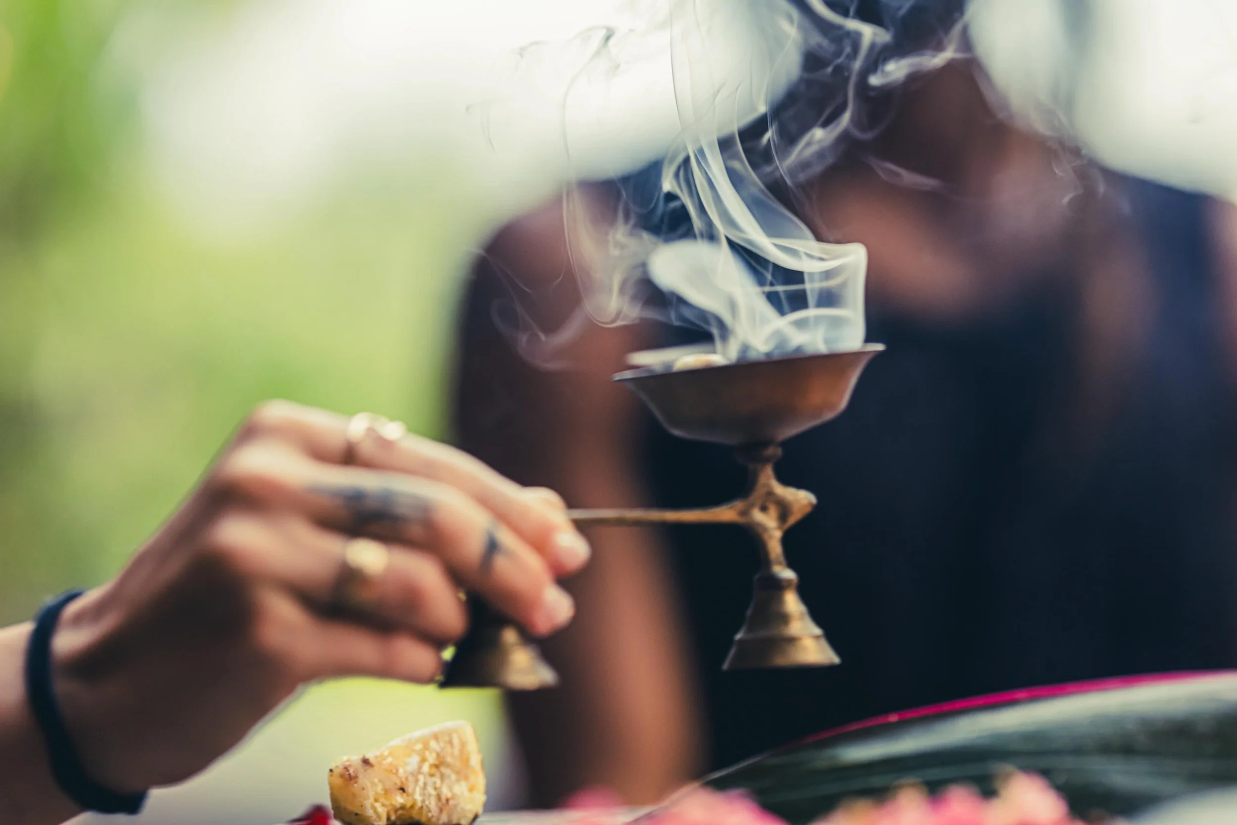 Person holding a brass oil lamp with smoke rising from it during a ritual or ceremony.