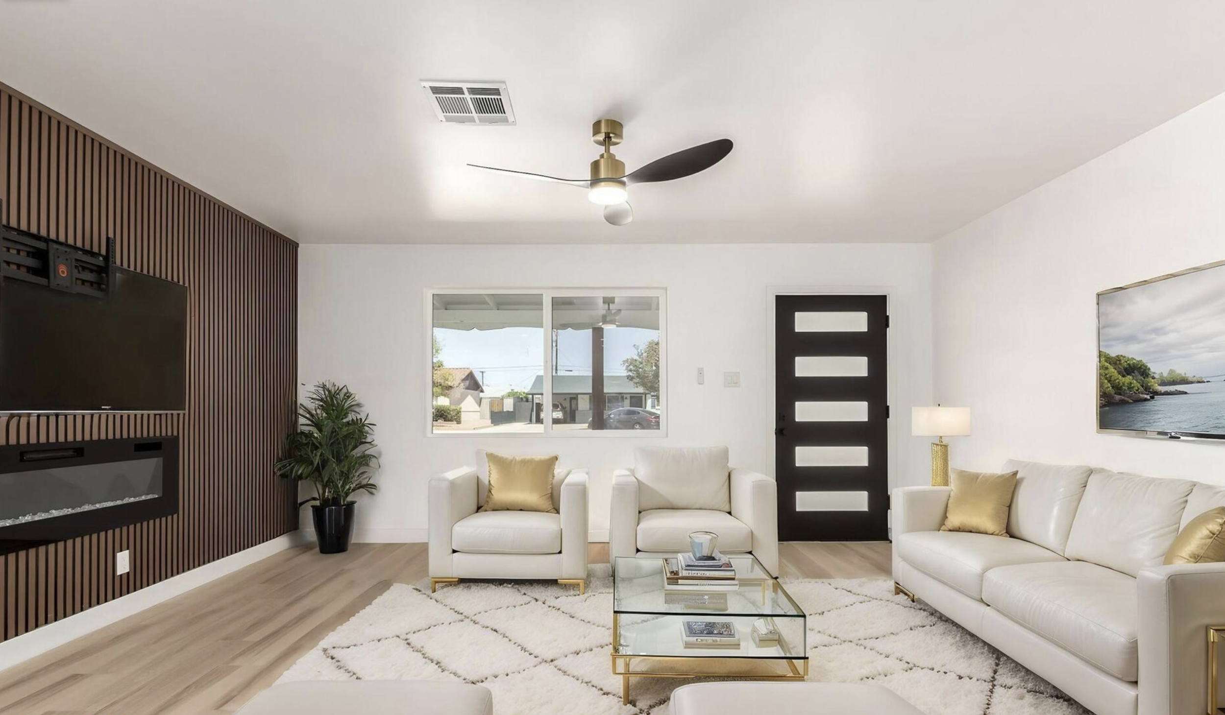 Modern living room with white sofas, gold pillows, glass coffee table, potted plant, and wall-mounted TV, with a front door and window revealing a neighborhood view. For sale Scottsdale Tarah Cook #1 realtor in 85257