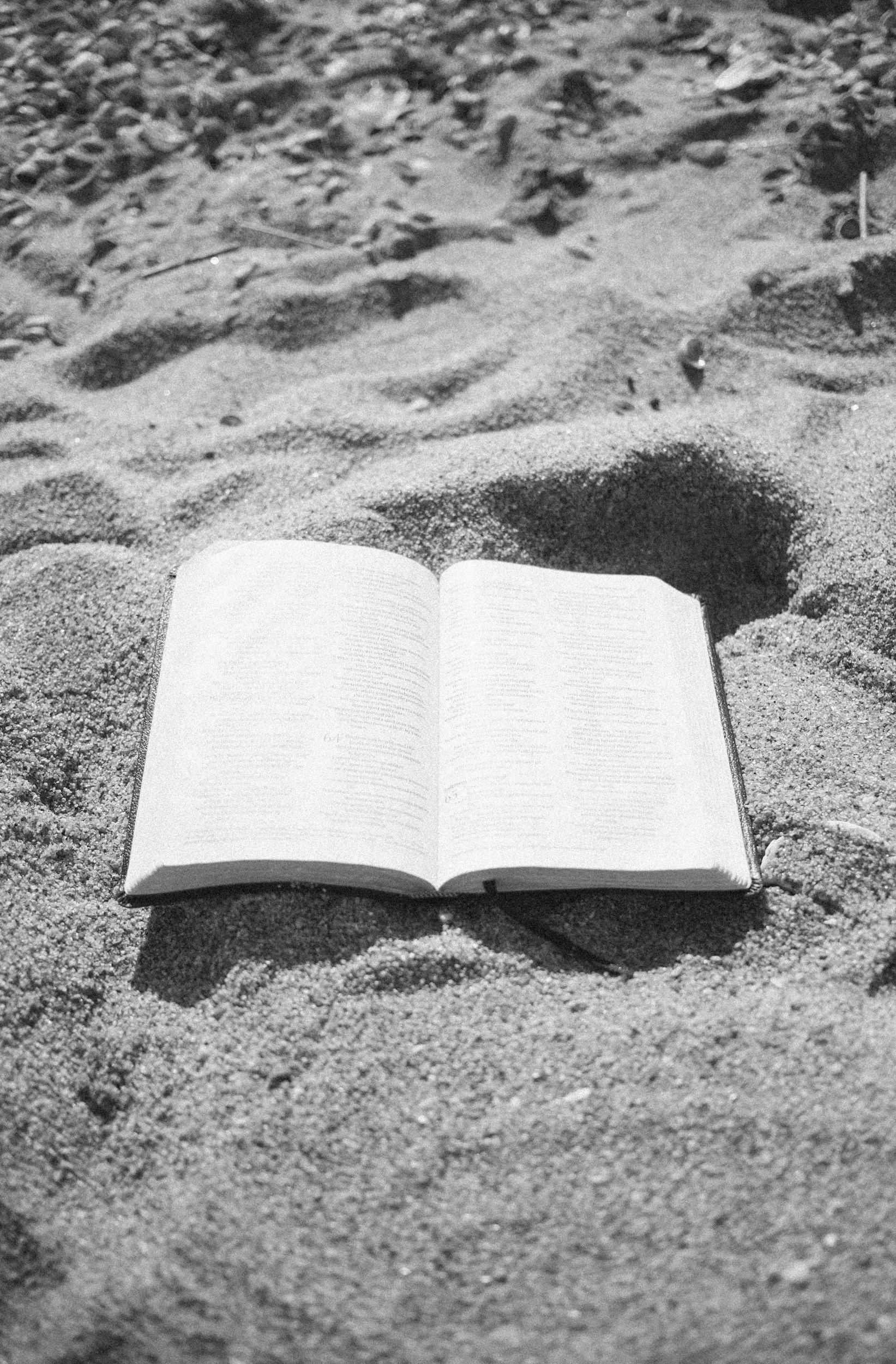 An open book resting on sandy ground at the beach.