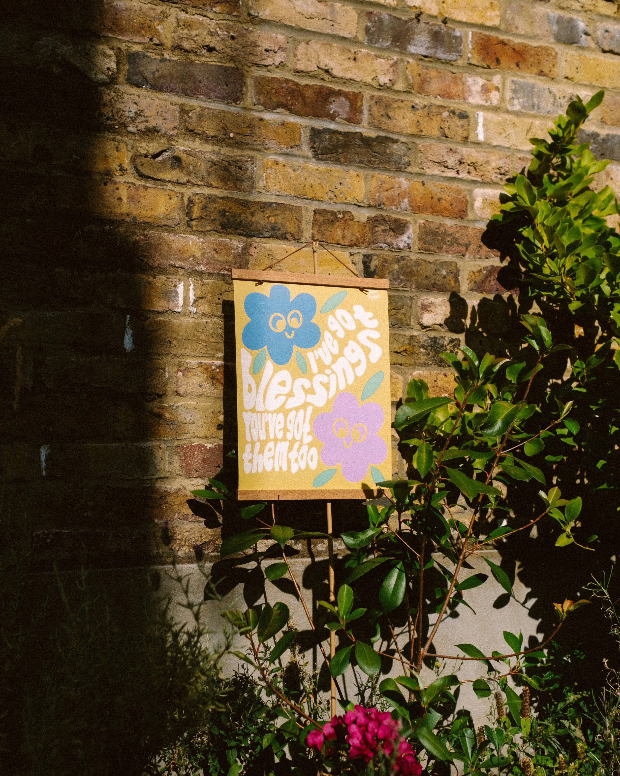 A colorful sign with cheerful flowers and the quote, "I’ve got so many reasons to love you" in playful lettering, placed among green plants and roses in front of a brick wall.