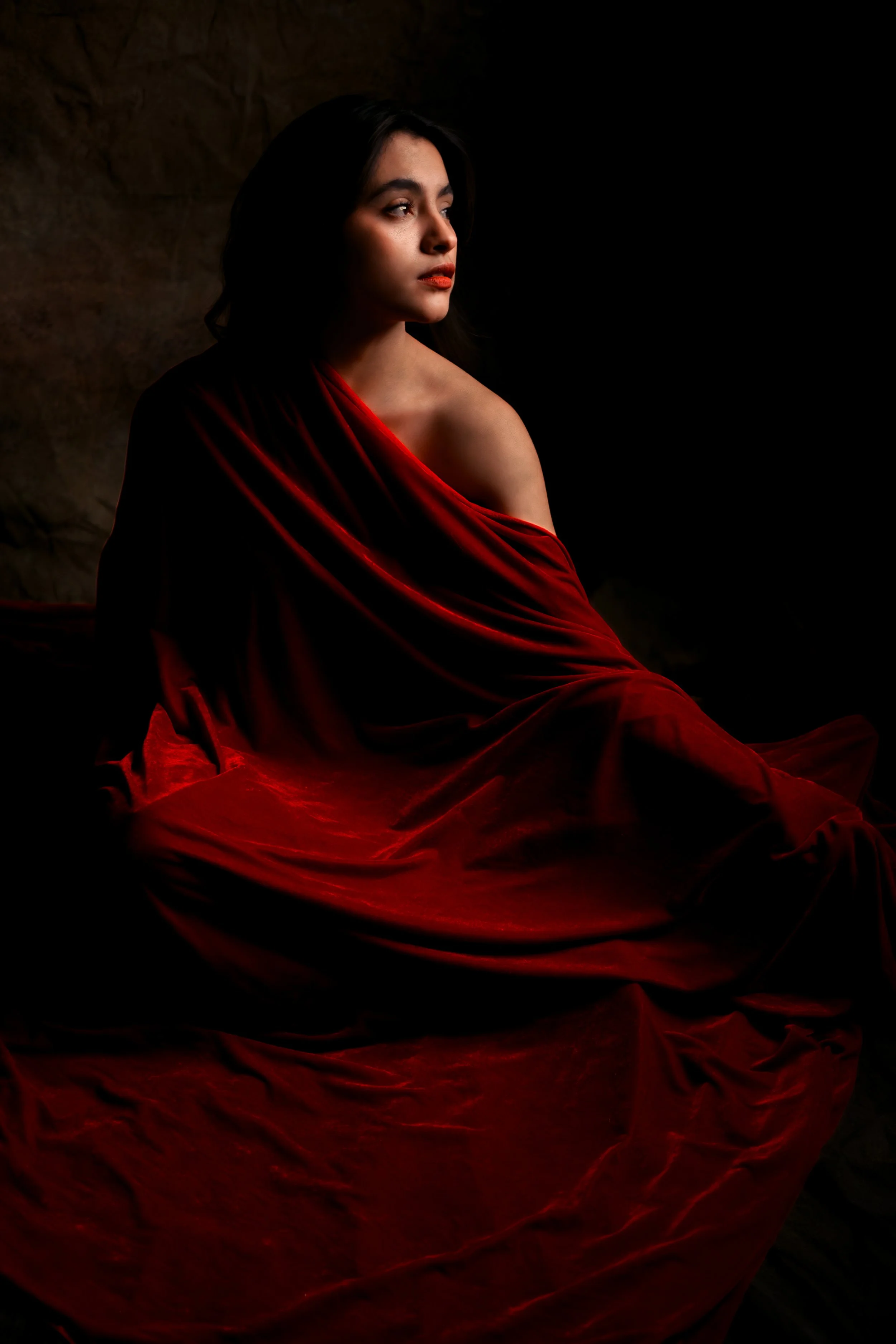Mujer con vestido rojo de seda, posando en un fondo oscuro, con expresión pensativa.
