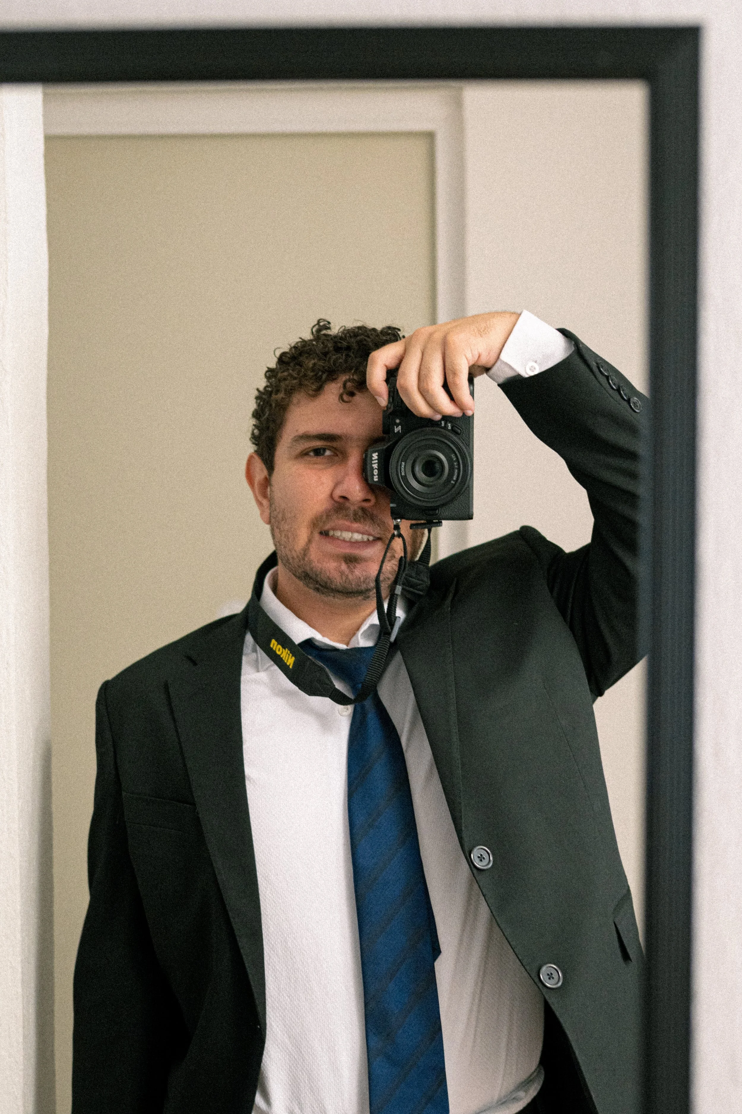 Joven con chaqueta y corbata tomando una selfie frente a un espejo.