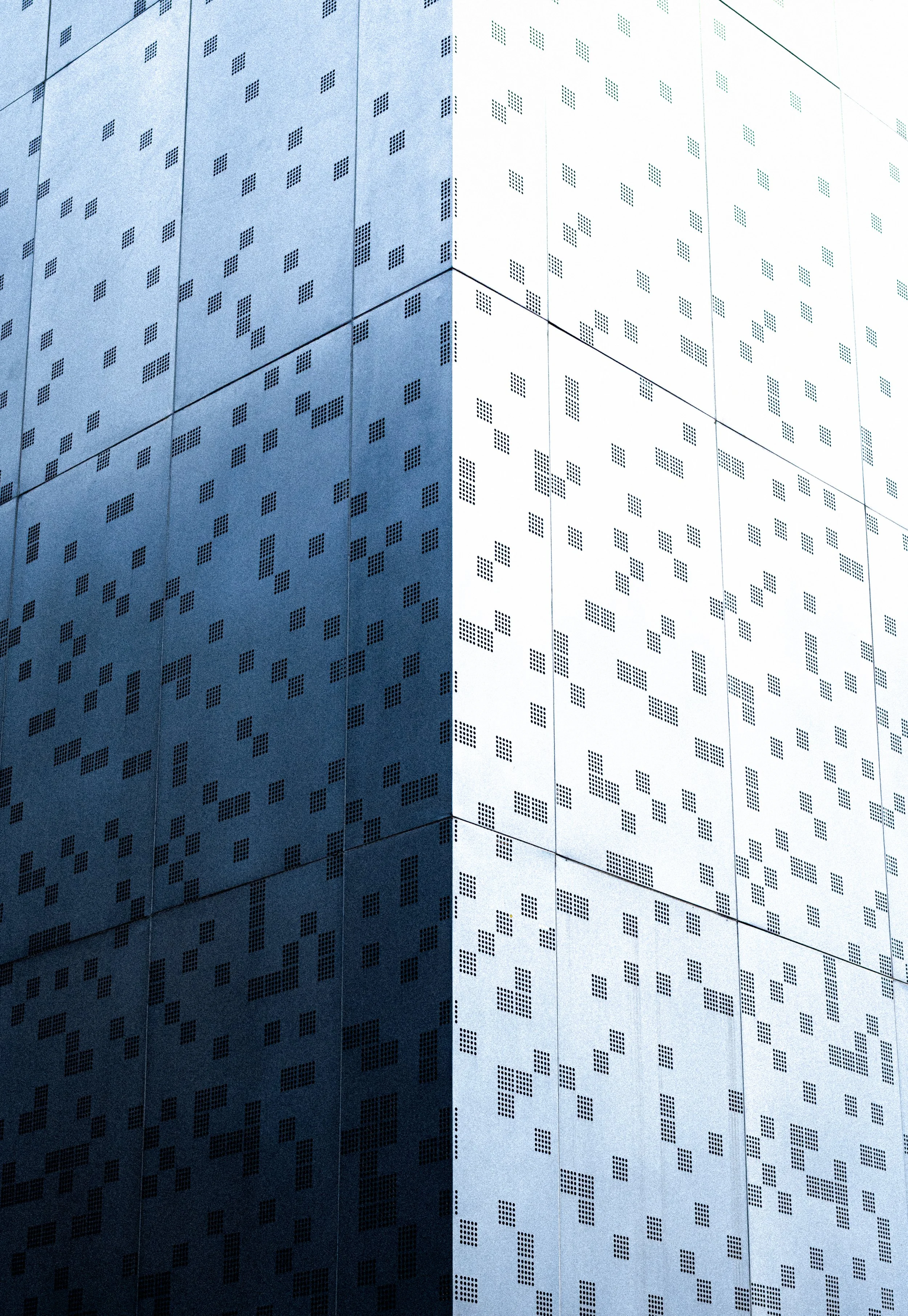 Pared de un edificio moderno con paneles metálicos y patrones de pequeños cuadrados en diferentes configuraciones