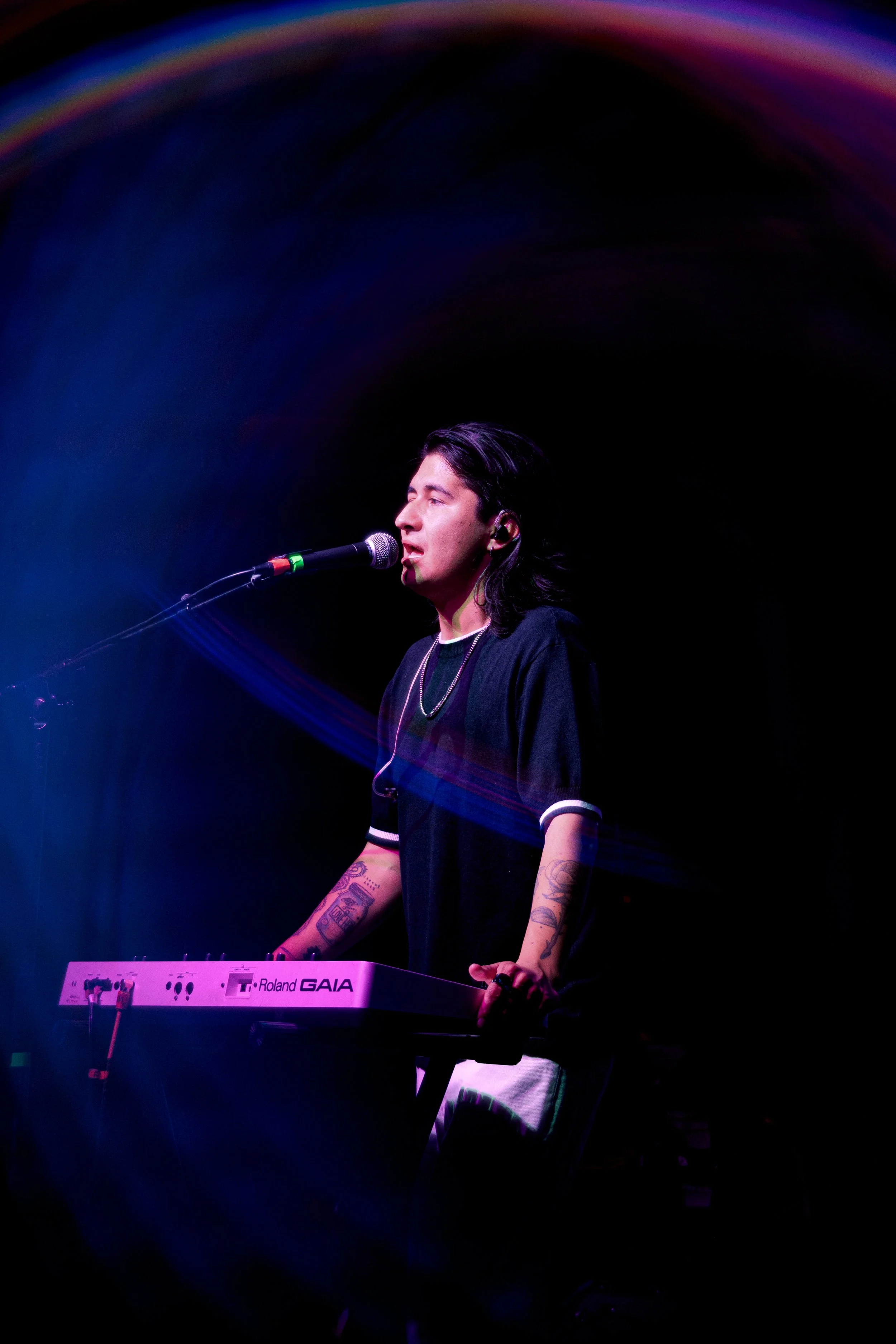 Joven tocando un teclado y cantando en un escenario con iluminación colorida.