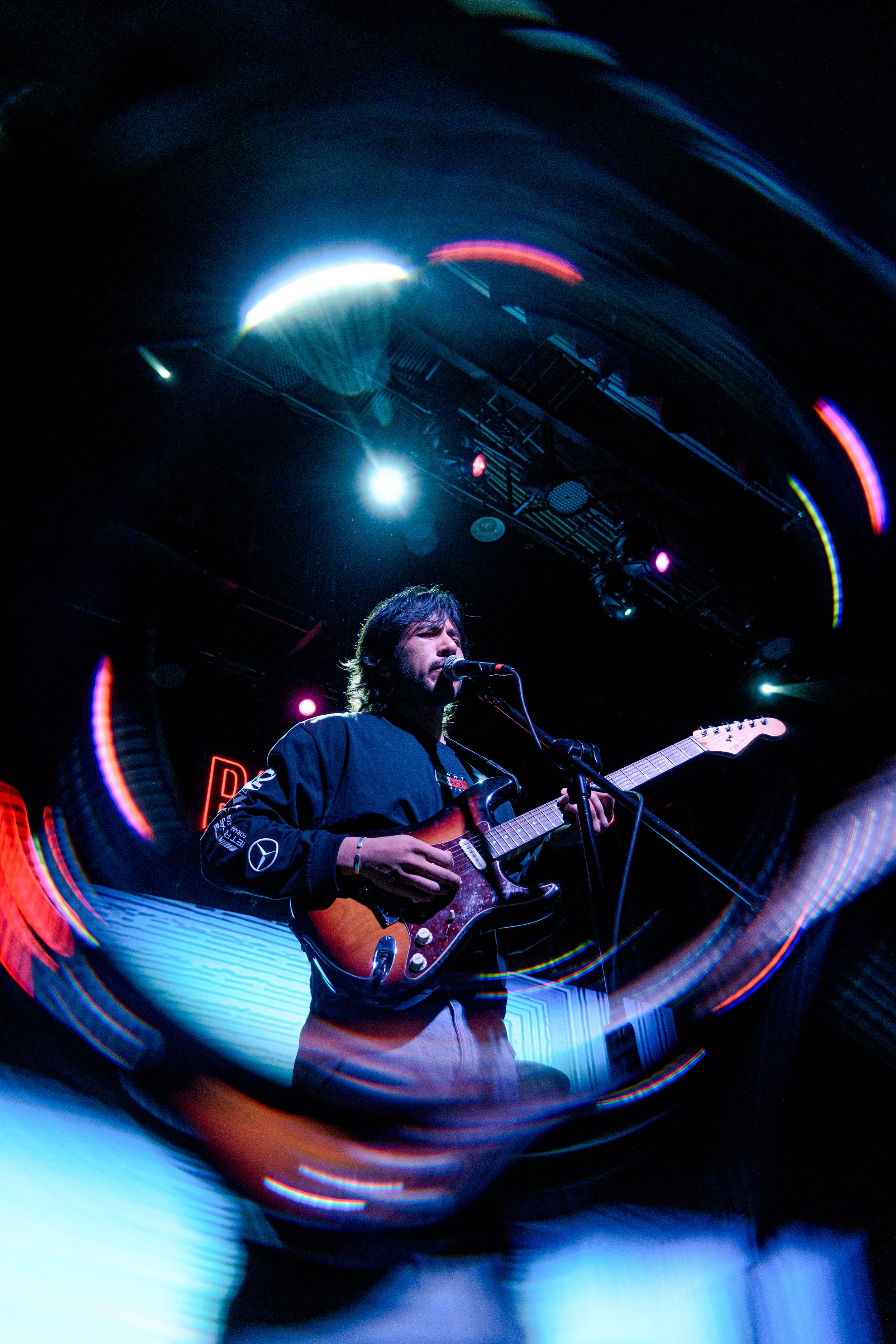 Persona tocando guitarra eléctrica en un escenario con iluminación vibrante.