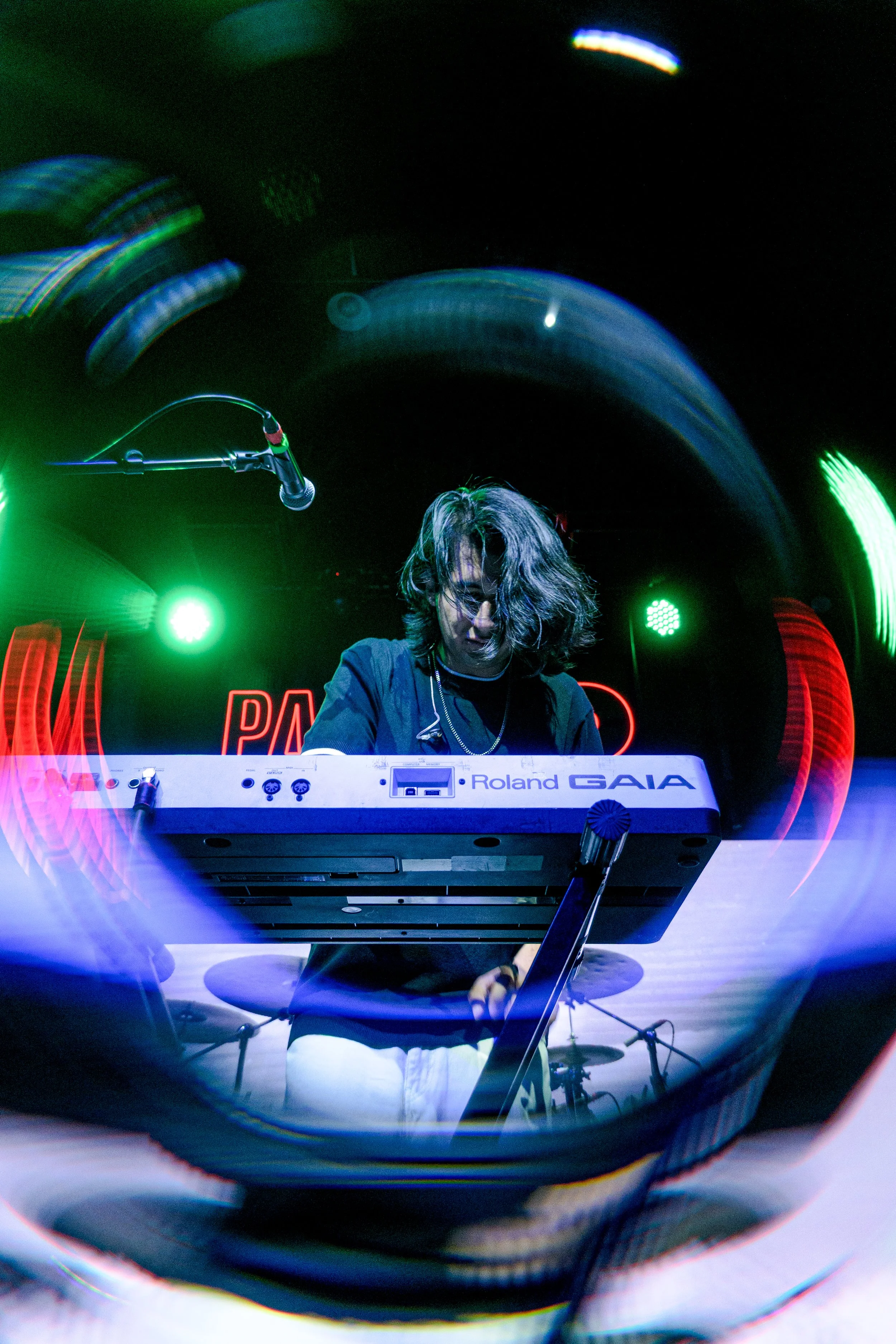 Una persona tocando un teclado en un escenario con luces verdes y rojas brillantes.