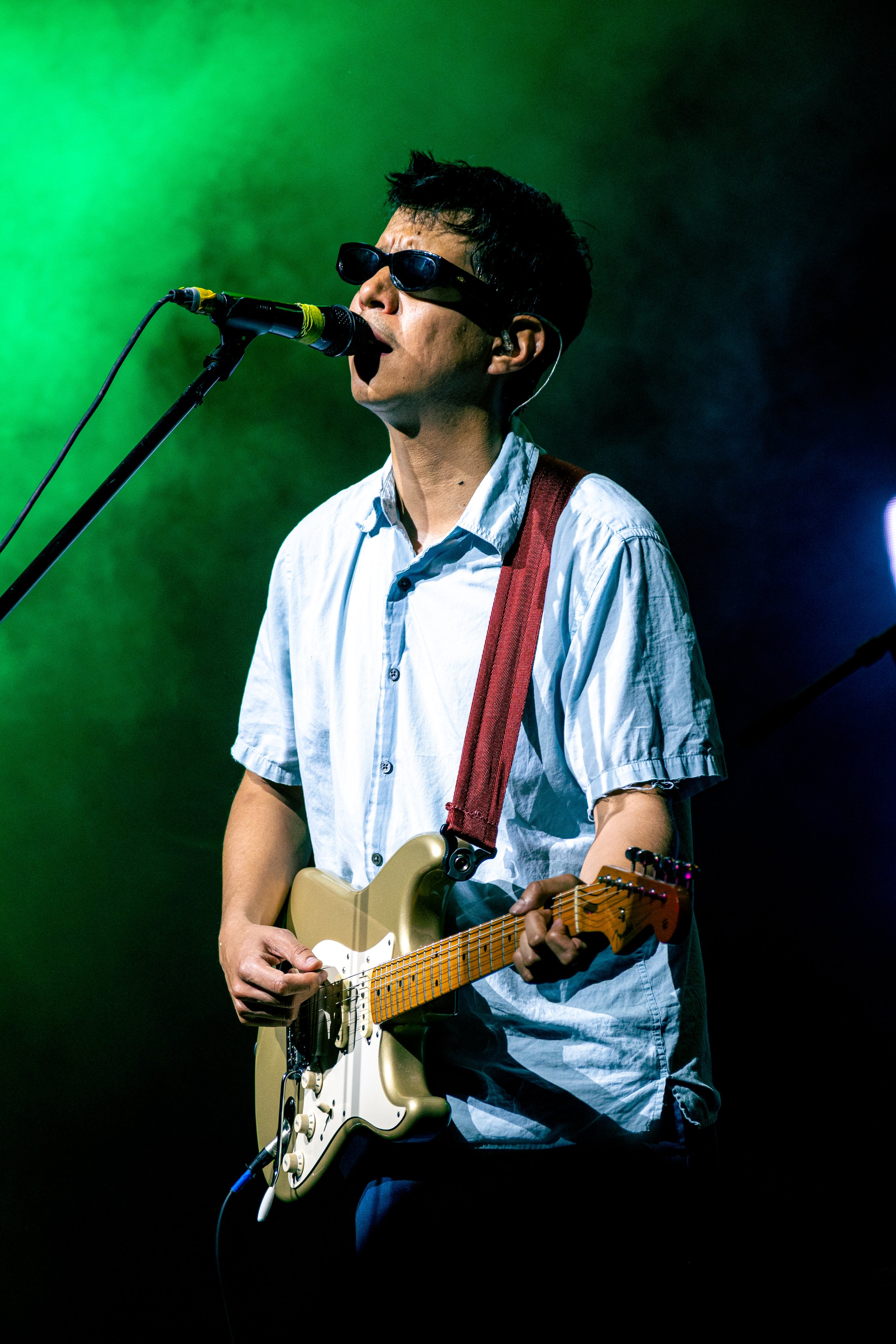 Joven tocando la guitarra eléctrica en un escenario con iluminación verde y negra.