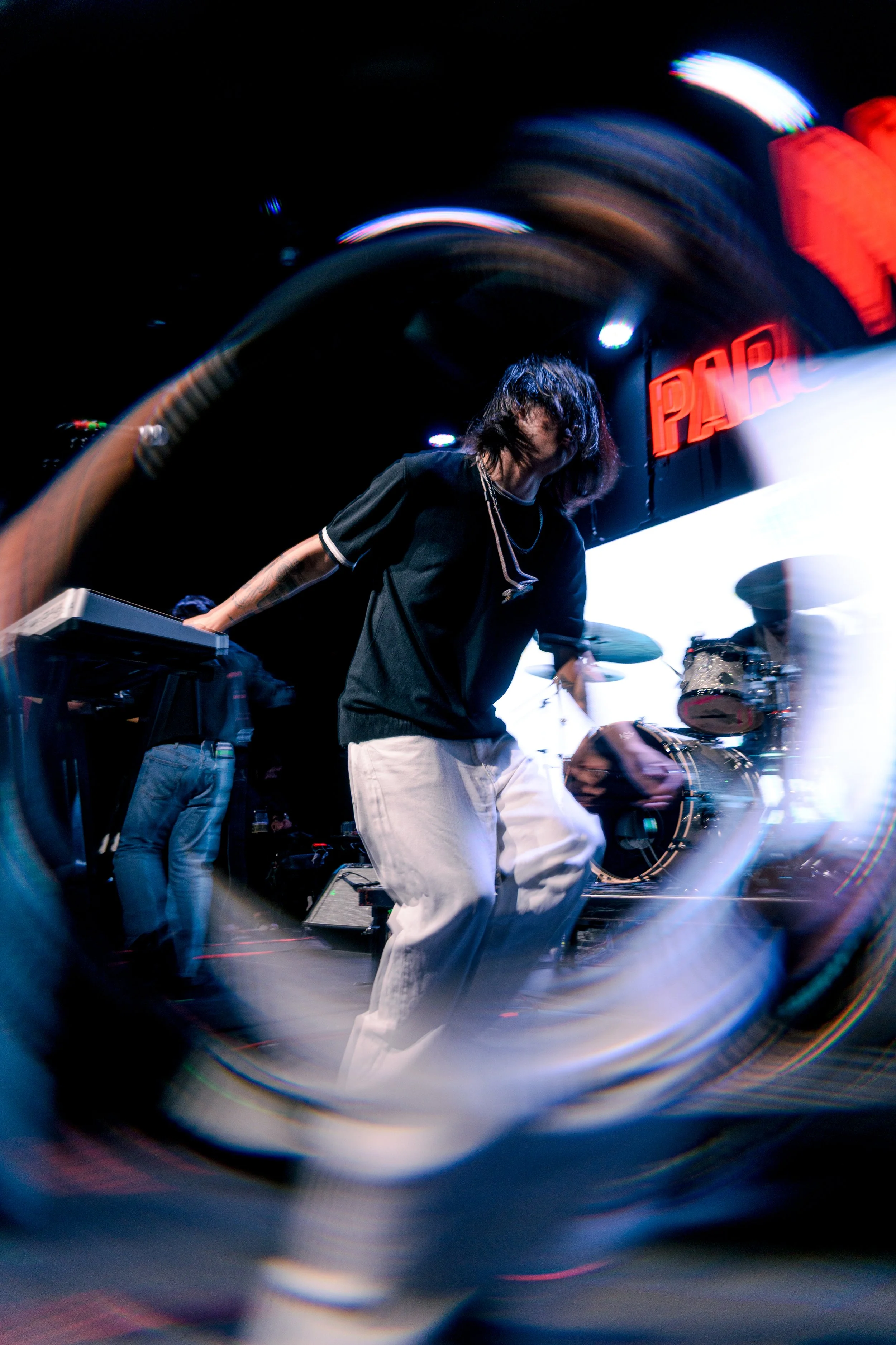 Un músico tocando en un escenario con iluminación y una señal de neón que dice 'PARK'.