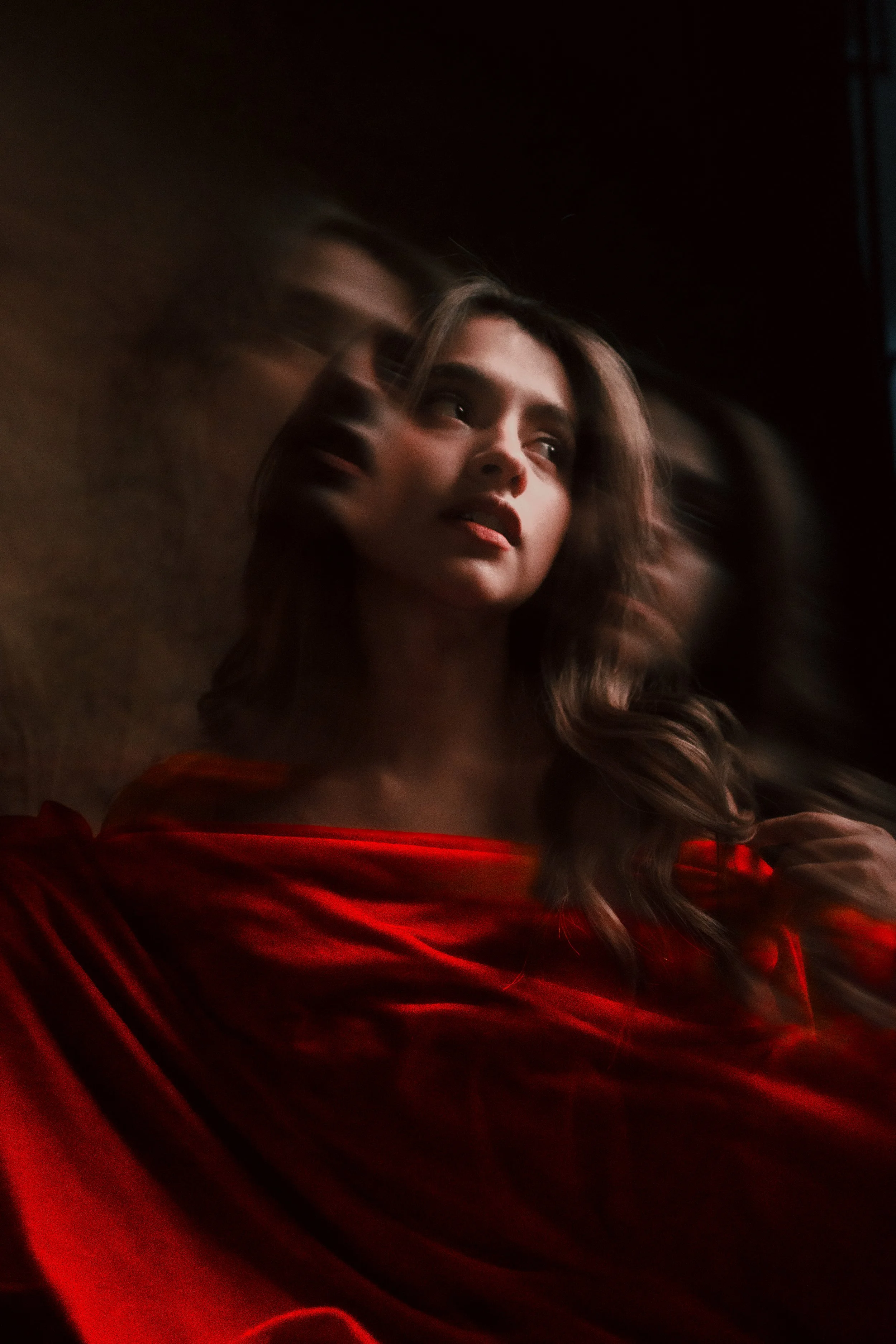 Retrato de una mujer con cabello rizado y largo, con vestido rojo, mirando hacia arriba en un ambiente oscuro.