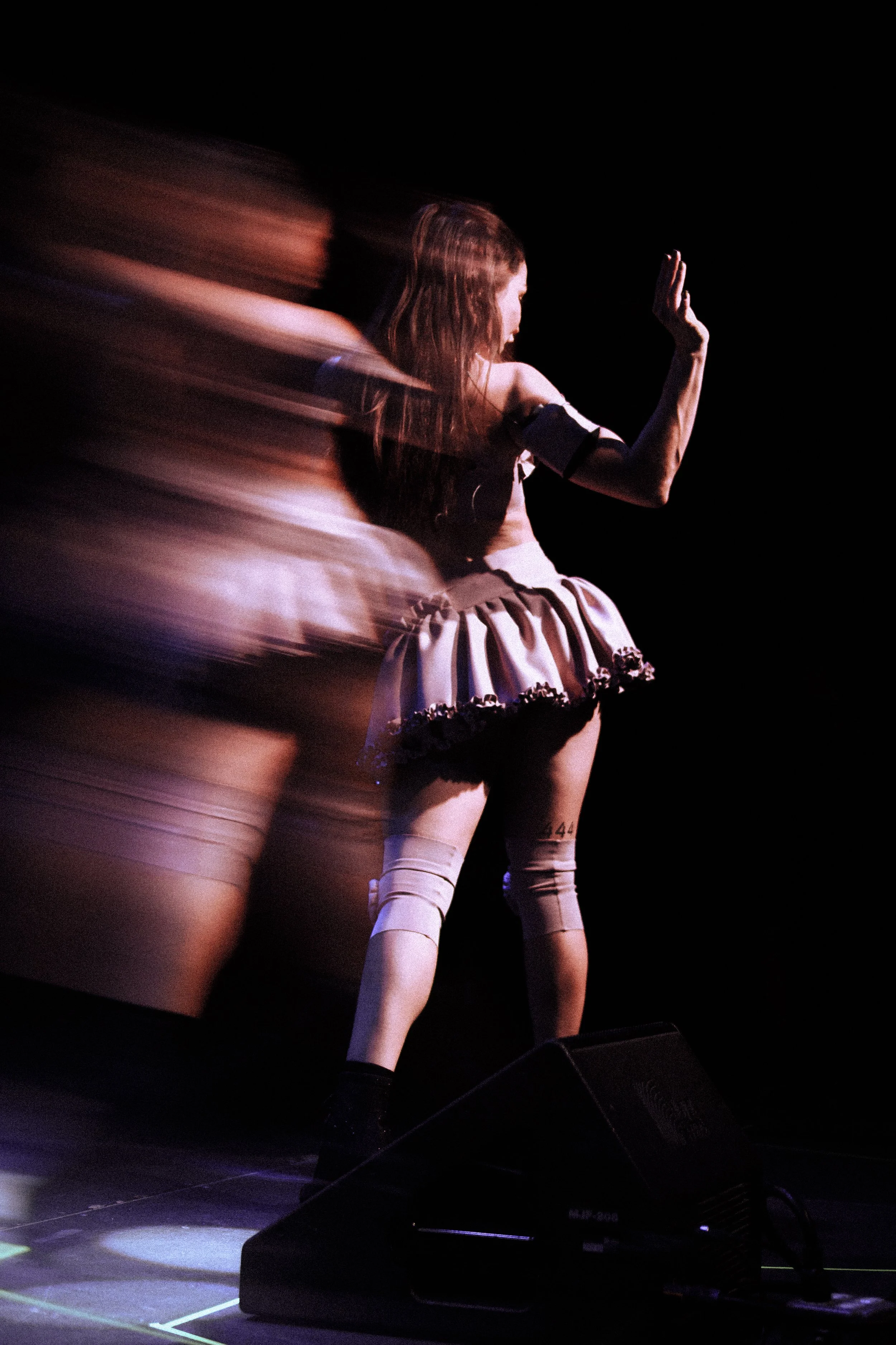 Una persona disfrazada de robot en un escenario con fondo negro, realizando un movimiento de baile o actuación, con efectos de movimiento difuso.