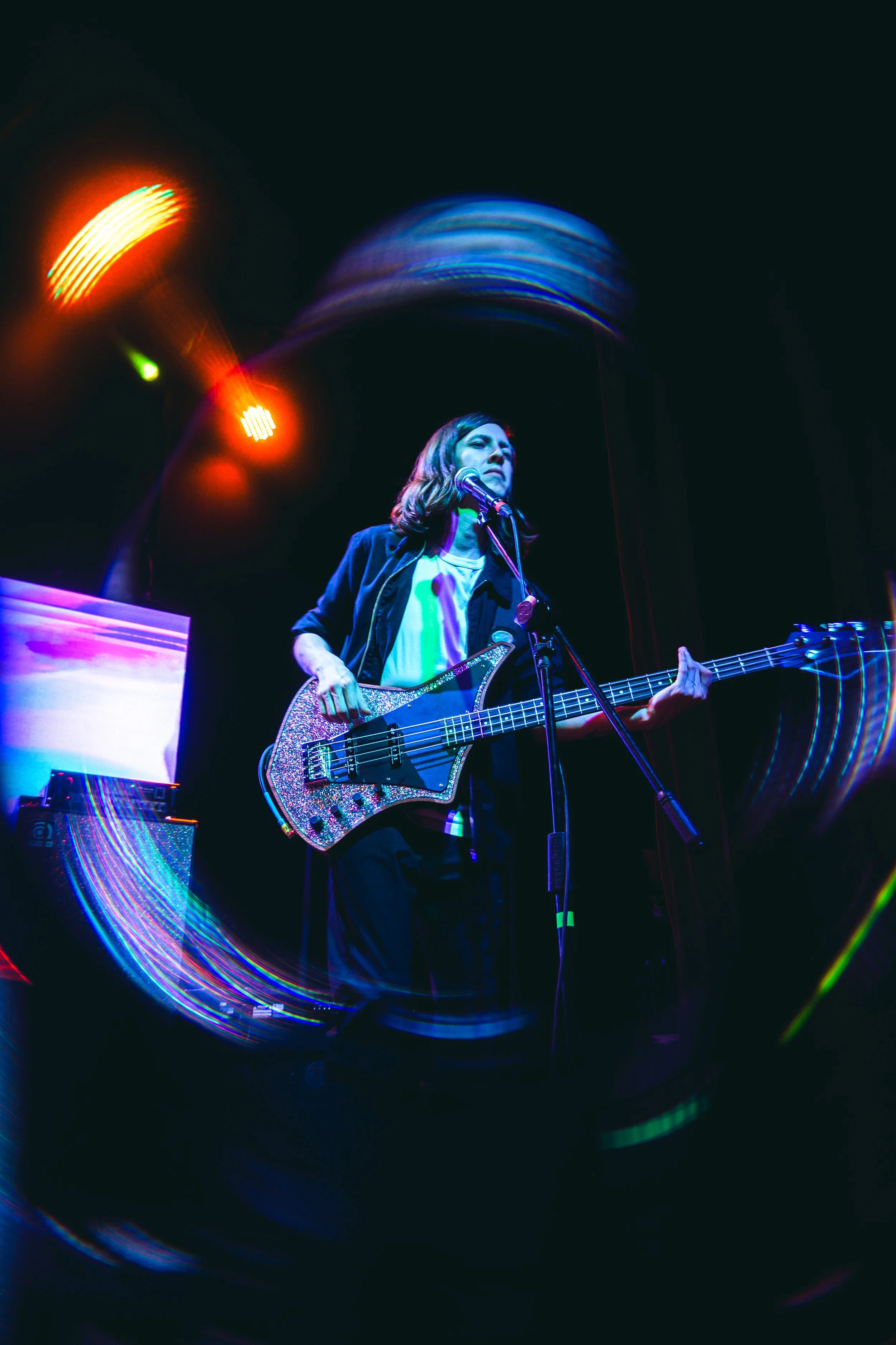 Una mujer tocando la guitarra eléctrica en un escenario con iluminación de colores y efectos de luz vibrantes.