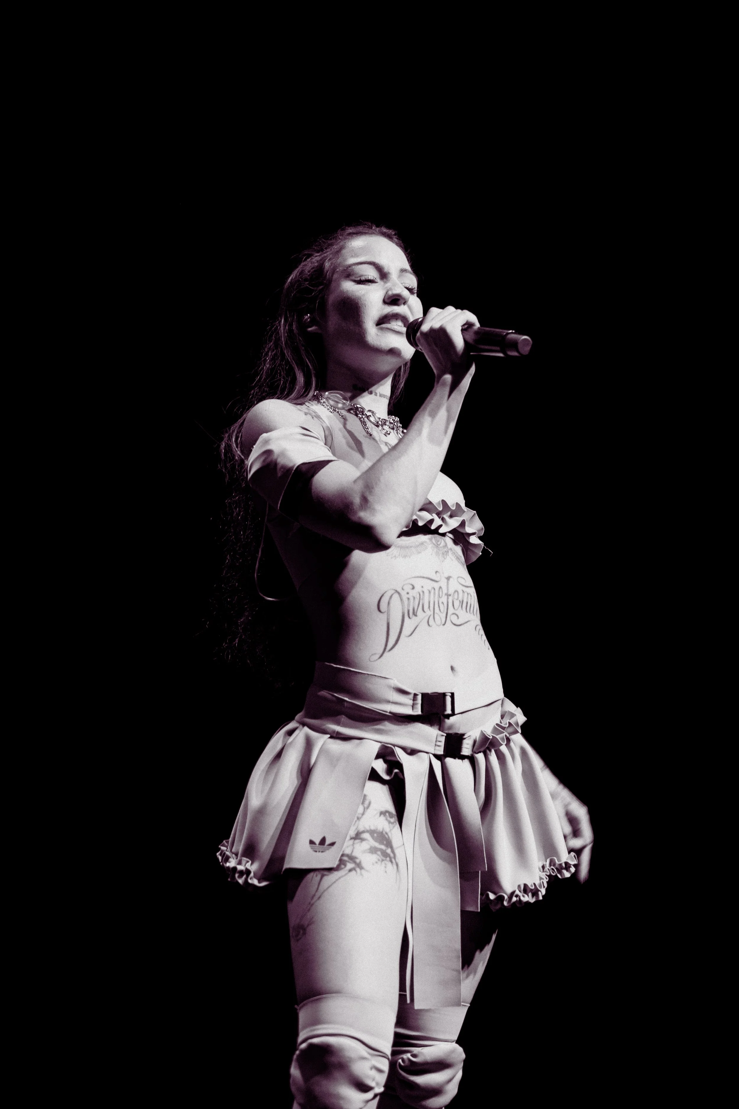 Una mujer cantando en un escenario con fondo negro, con expresión emocional y sosteniendo un micrófono.