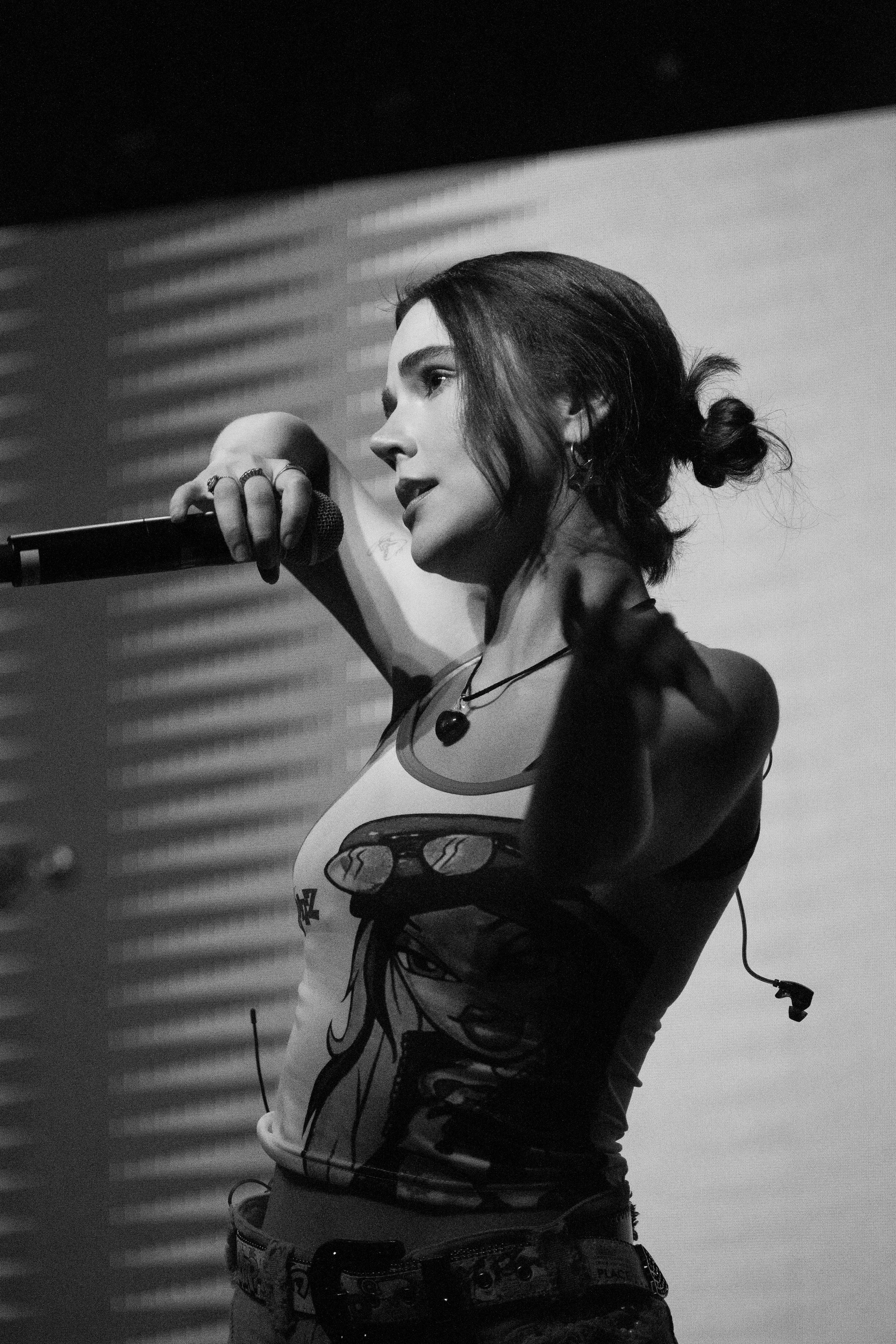 Mujer cantando o hablando en un micrófono en un escenario, en blanco y negro.