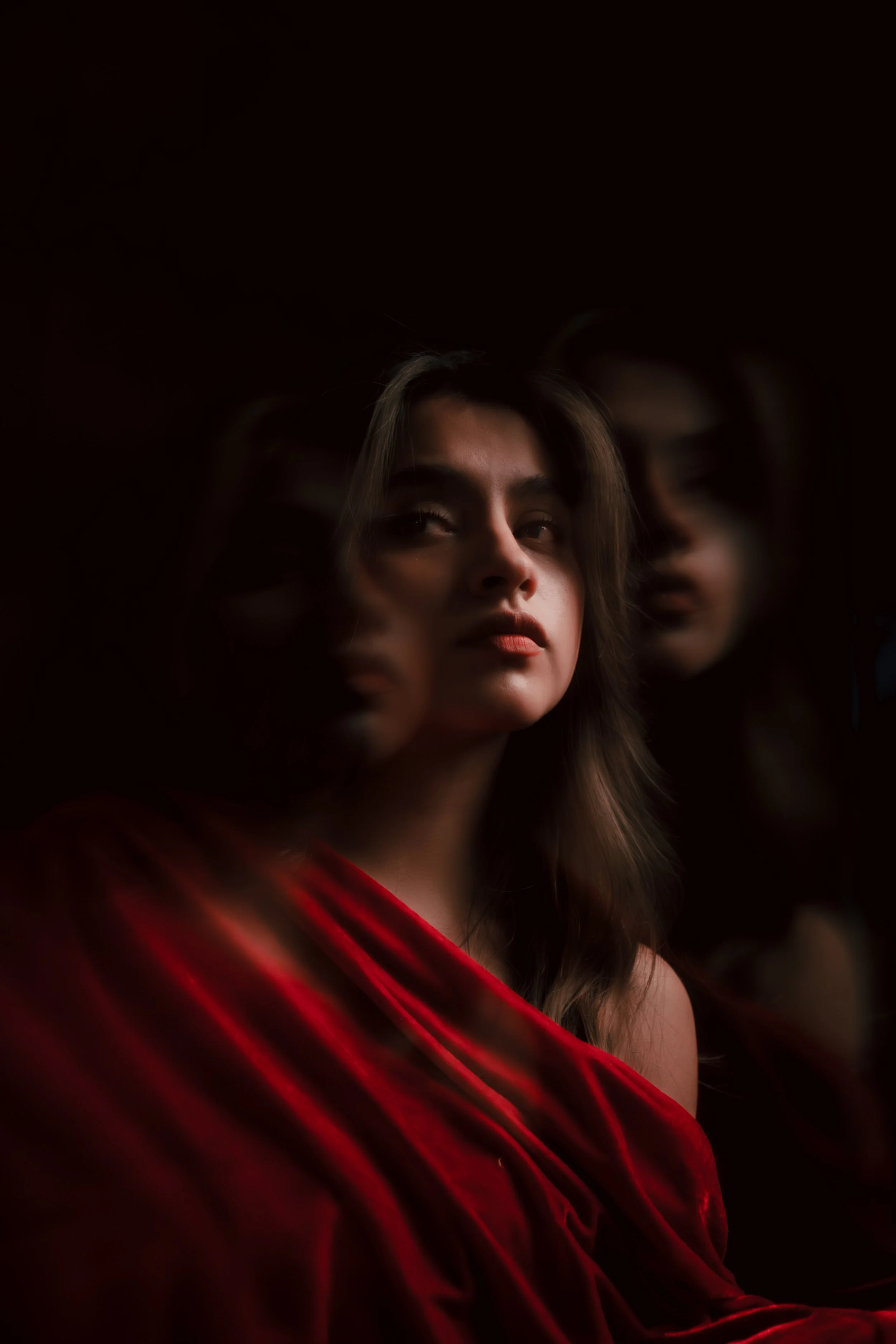 Retrato de una mujer con vestido rojo, con reflejos de su rostro en un espejo, en un ambiente oscuro.