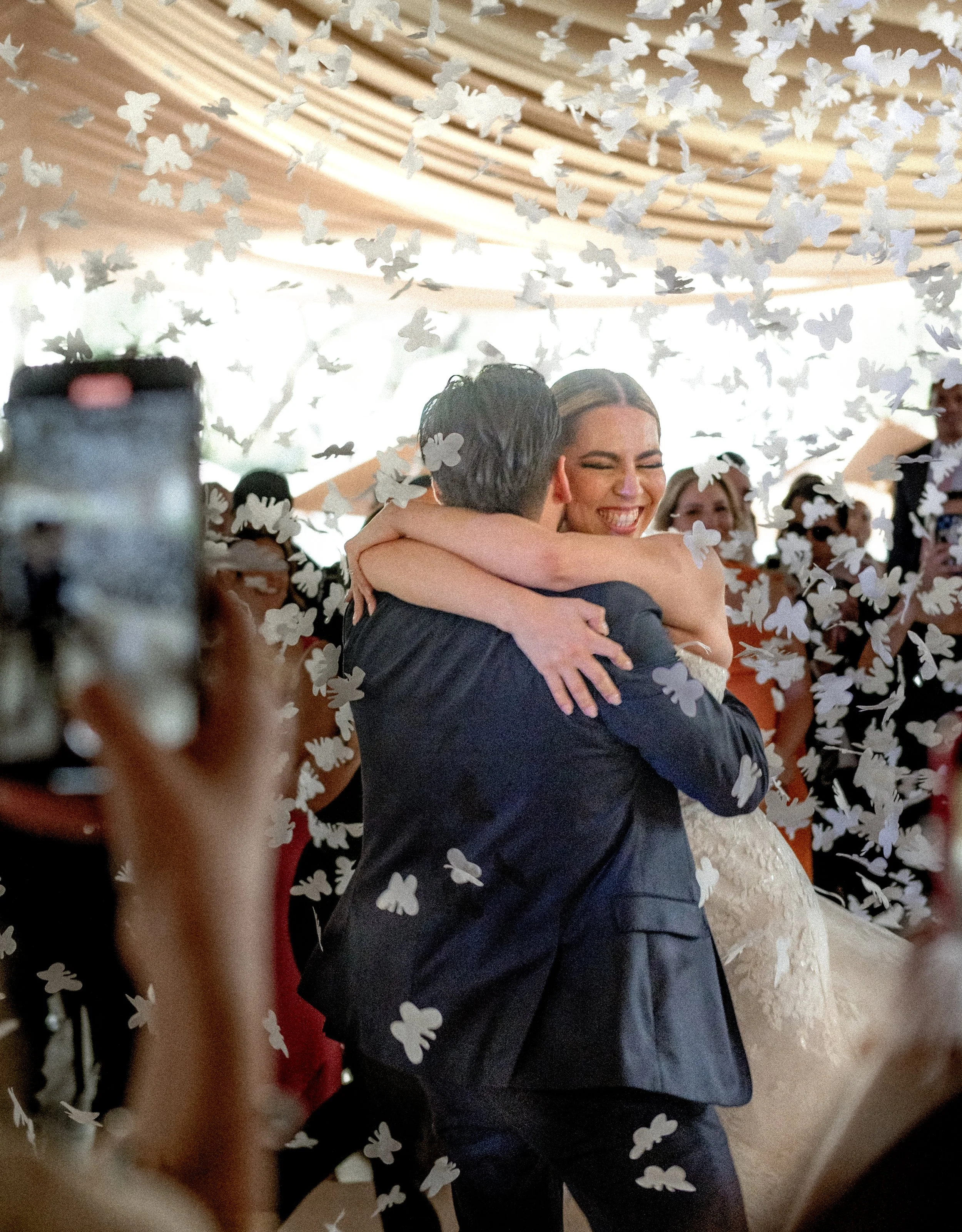 Pareja bailando y abrazándose durante una celebración con confeti de mariposas en un ambiente festivo.
