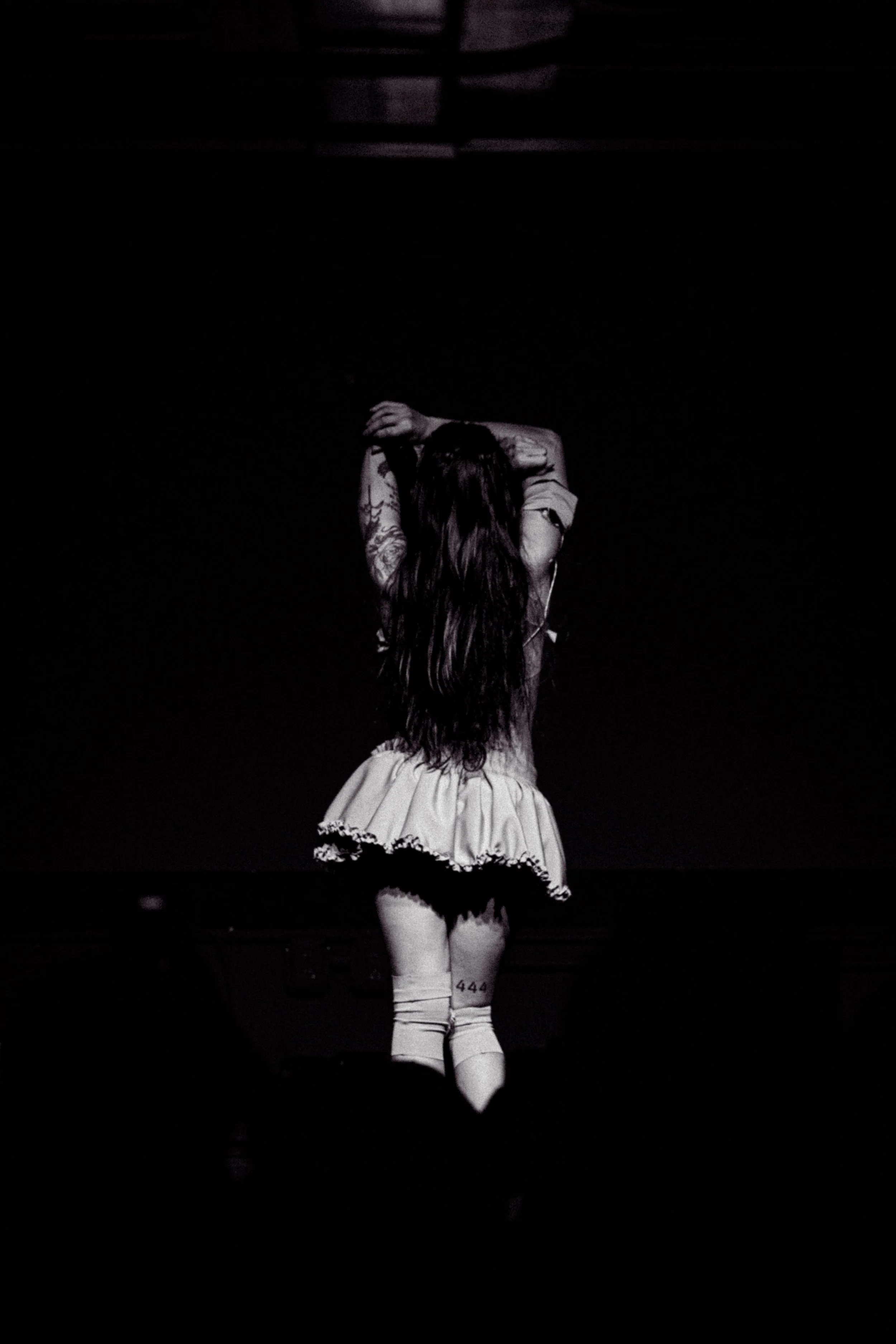 Mujer con cabello largo y oscuro, vestido corto y calcetines altos en un escenario oscuro.