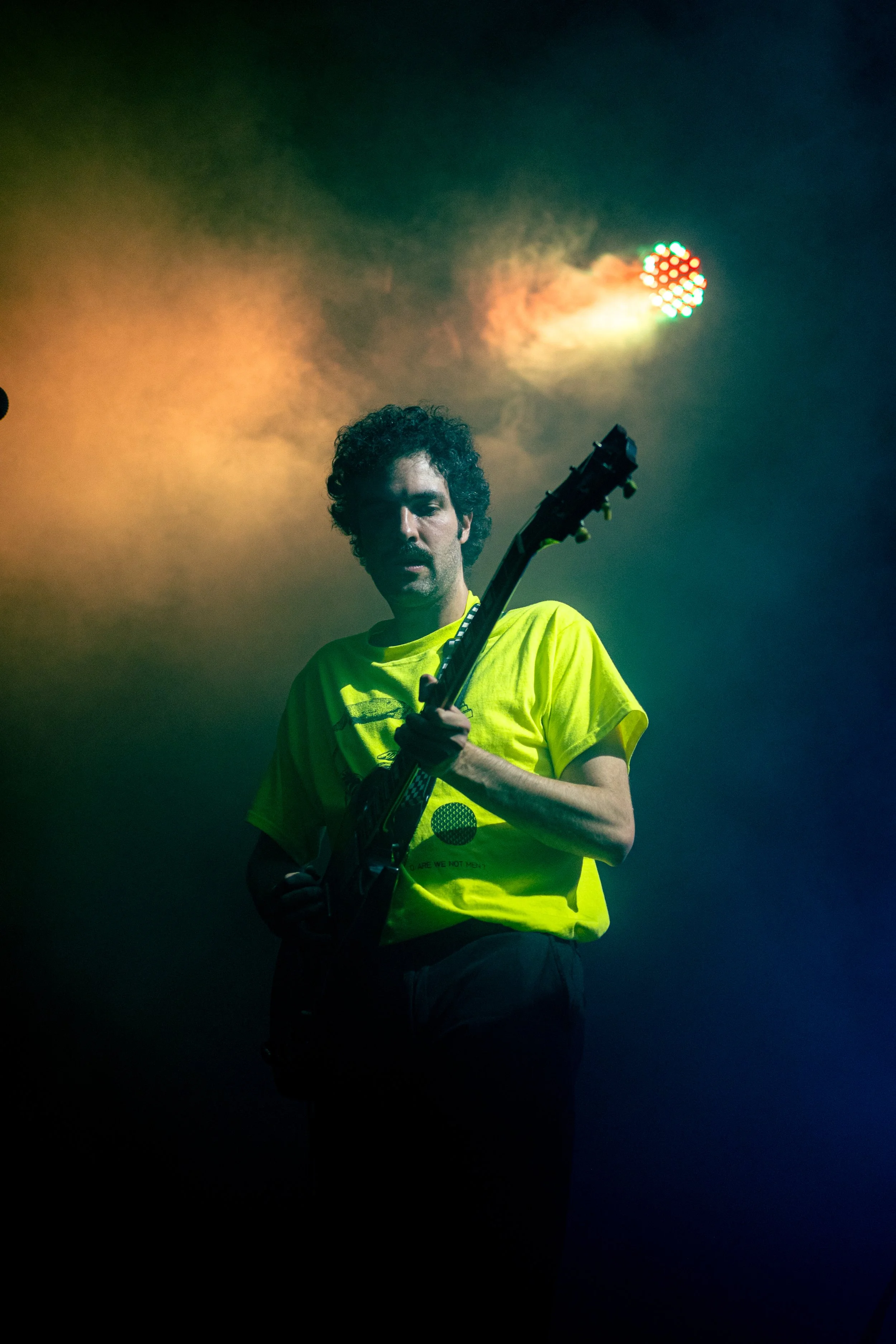 Hombre tocando la guitarra en un escenario con luces multicolores y humo.