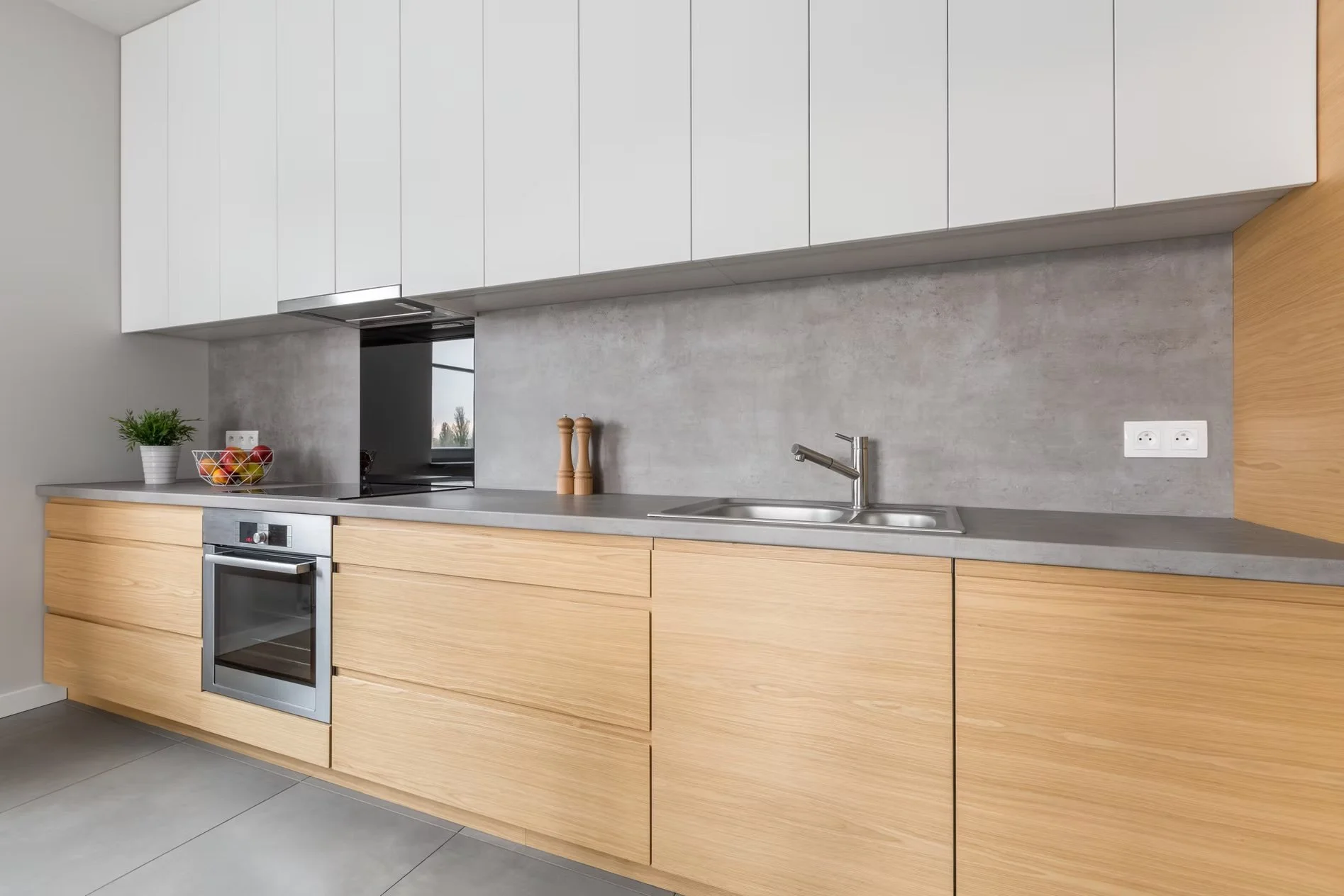 Cocina moderna con gabinetes de madera clara, encimera de concreto, electrodomésticos integrados y accesorios sencillos.