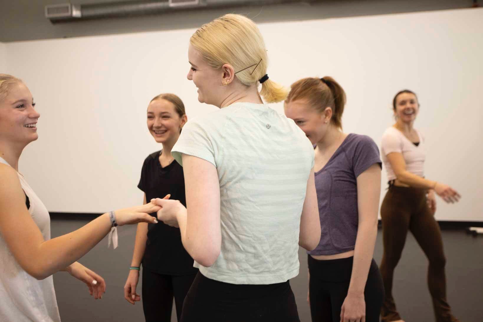 Group of young women laughing and talking in a dance studi setting.