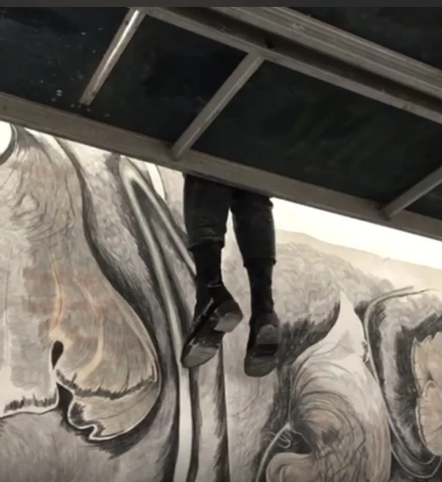 Benen die onder een stijger bungelen en op de muur een kunstwerk