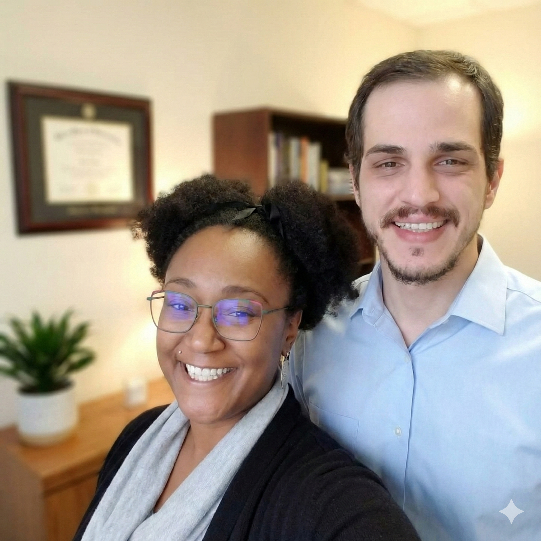 Smiling bookkeeper wearing glasses standing beside a colleague in a professional office setting.