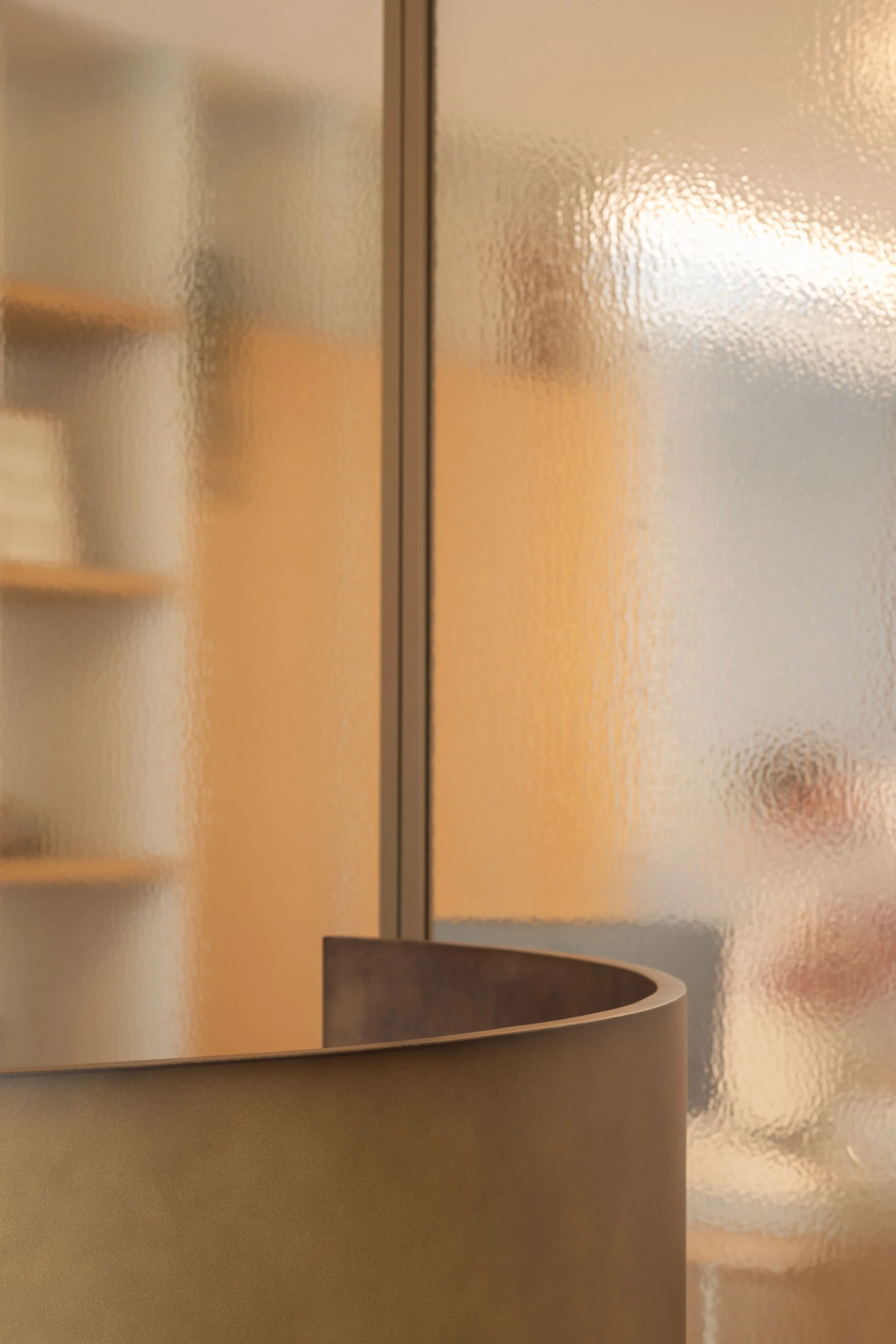 Een detailopname van een gebogen bronzen balie voor een wand van mat figuurglas met een strak metalen profiel.