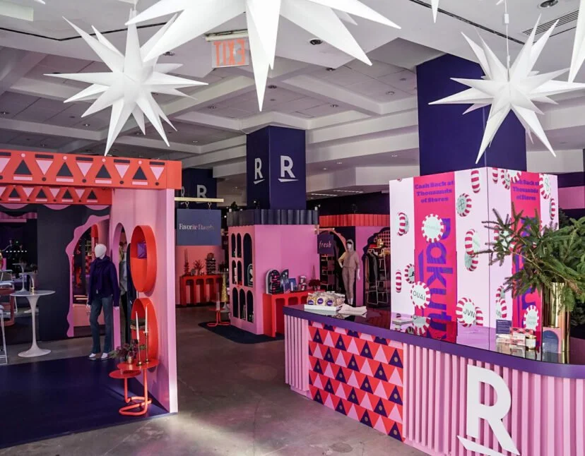 Colorful retail pop-up store with pink, purple, and red decorations, display shelves, and large white star-shaped hanging decorations.