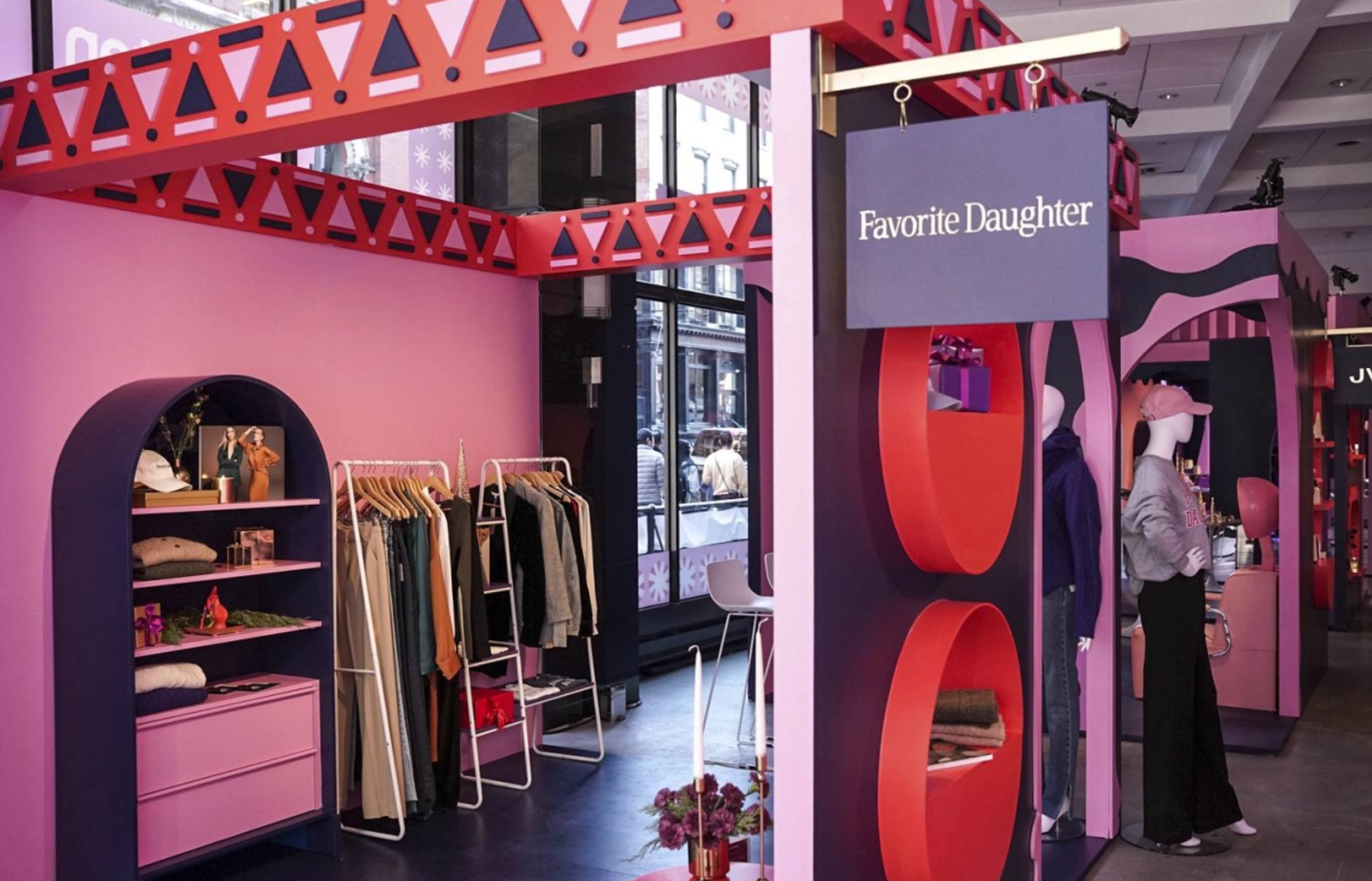 Interior of a retail store decorated in pink and purple with clothing racks, mannequins, and festive decorations, including a sign that reads 'Favorite Daughter'.